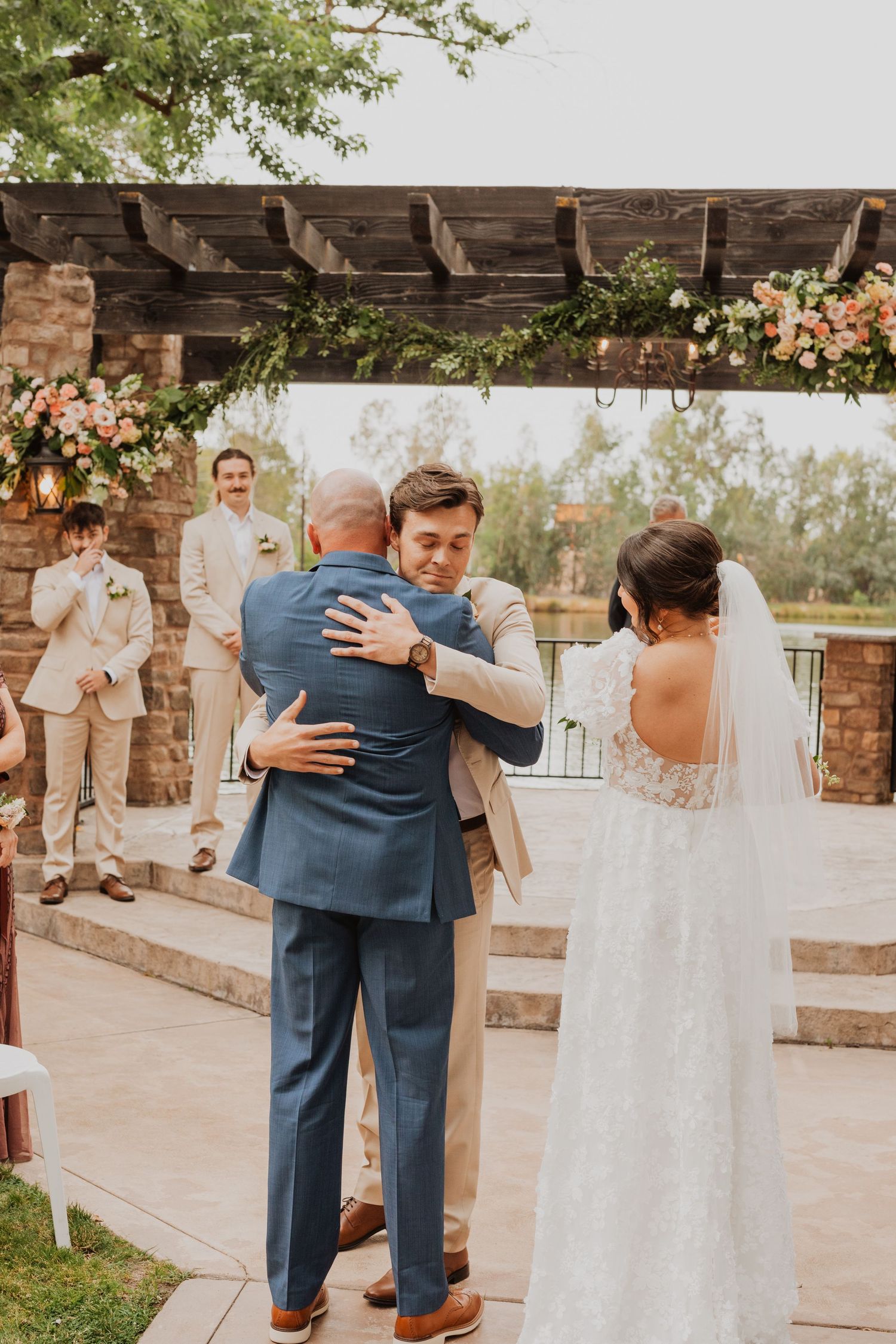 Emotional moments during outdoor wedding ceremony under wooden pergola with stone pillars.
