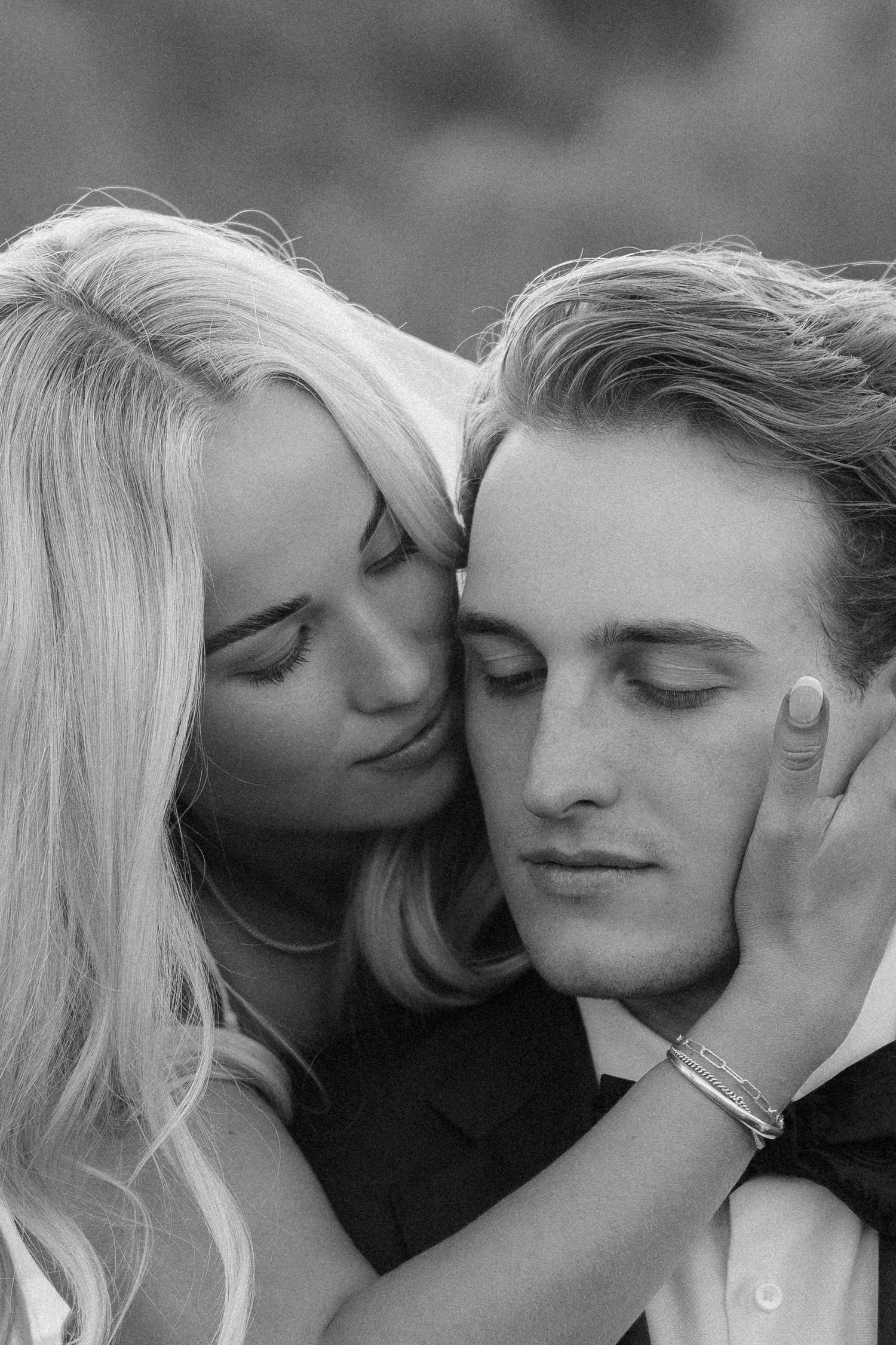 Black and white romantic couple portrait with woman embracing man from behind, both with eyes closed in tender moment.