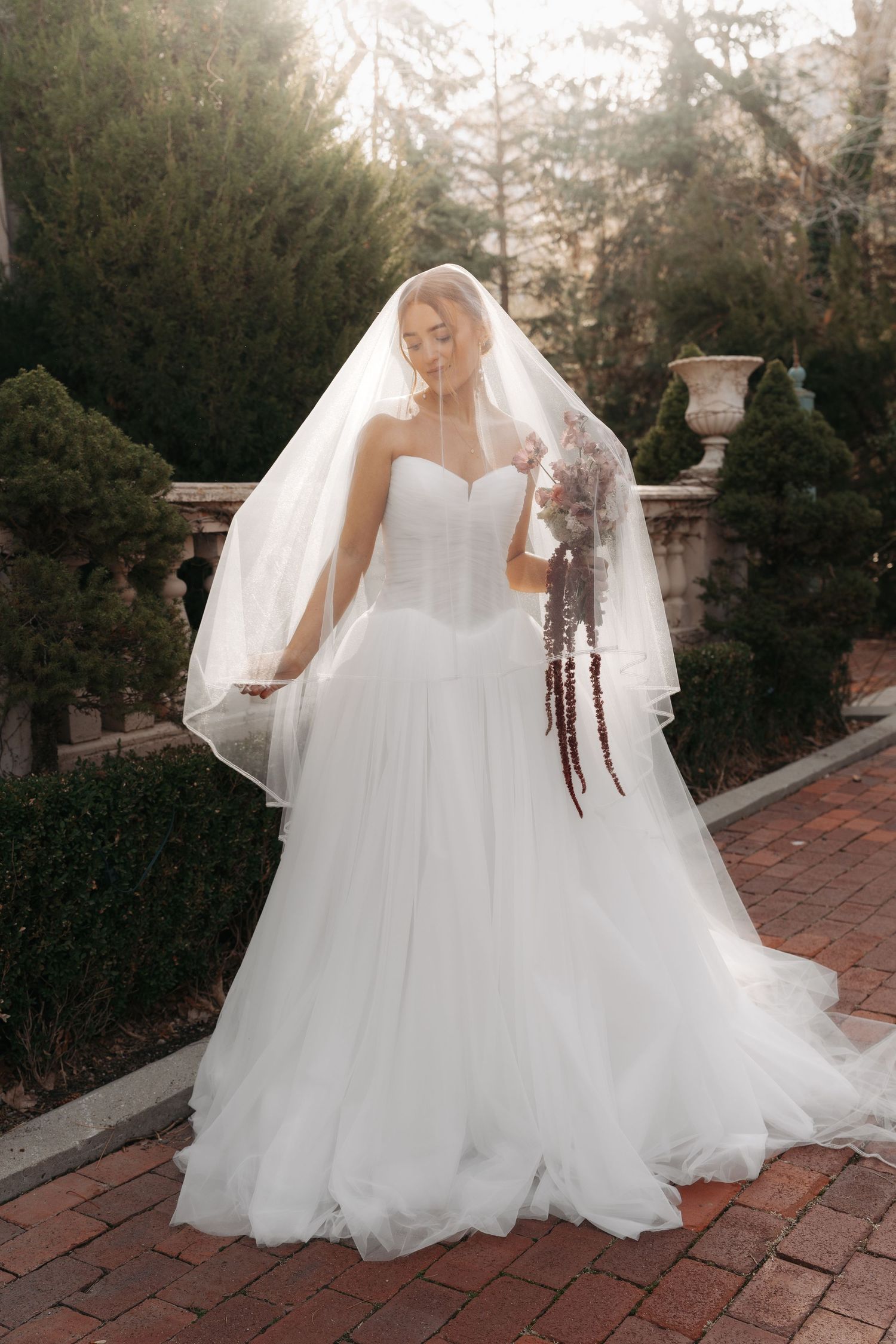 Bride in strapless ballgown and veil poses on brick path at sunset.
