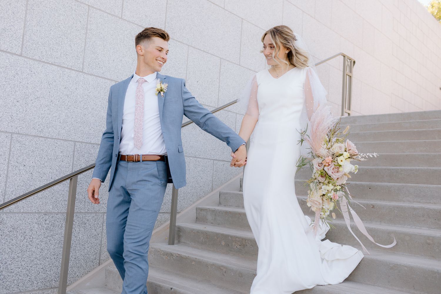 Wedding couple walking up stone steps in elegant attire.