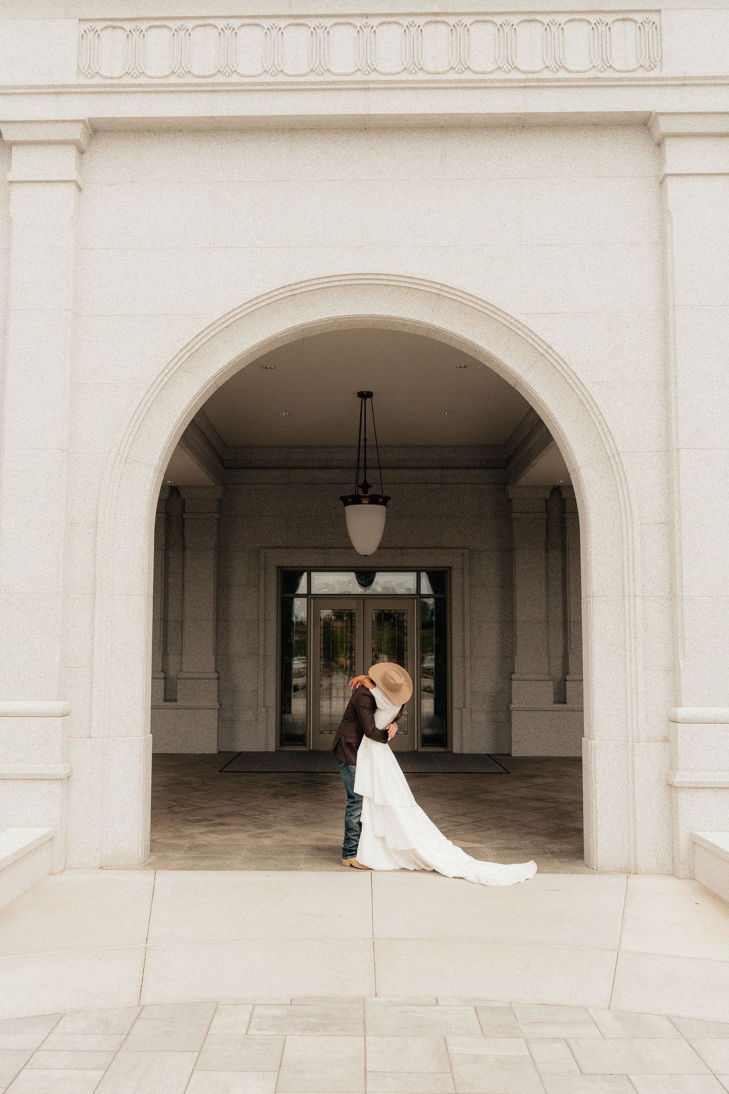 Bride and groom sharing a romantic kiss under an elegant white stone arch at a classic wedding venue.