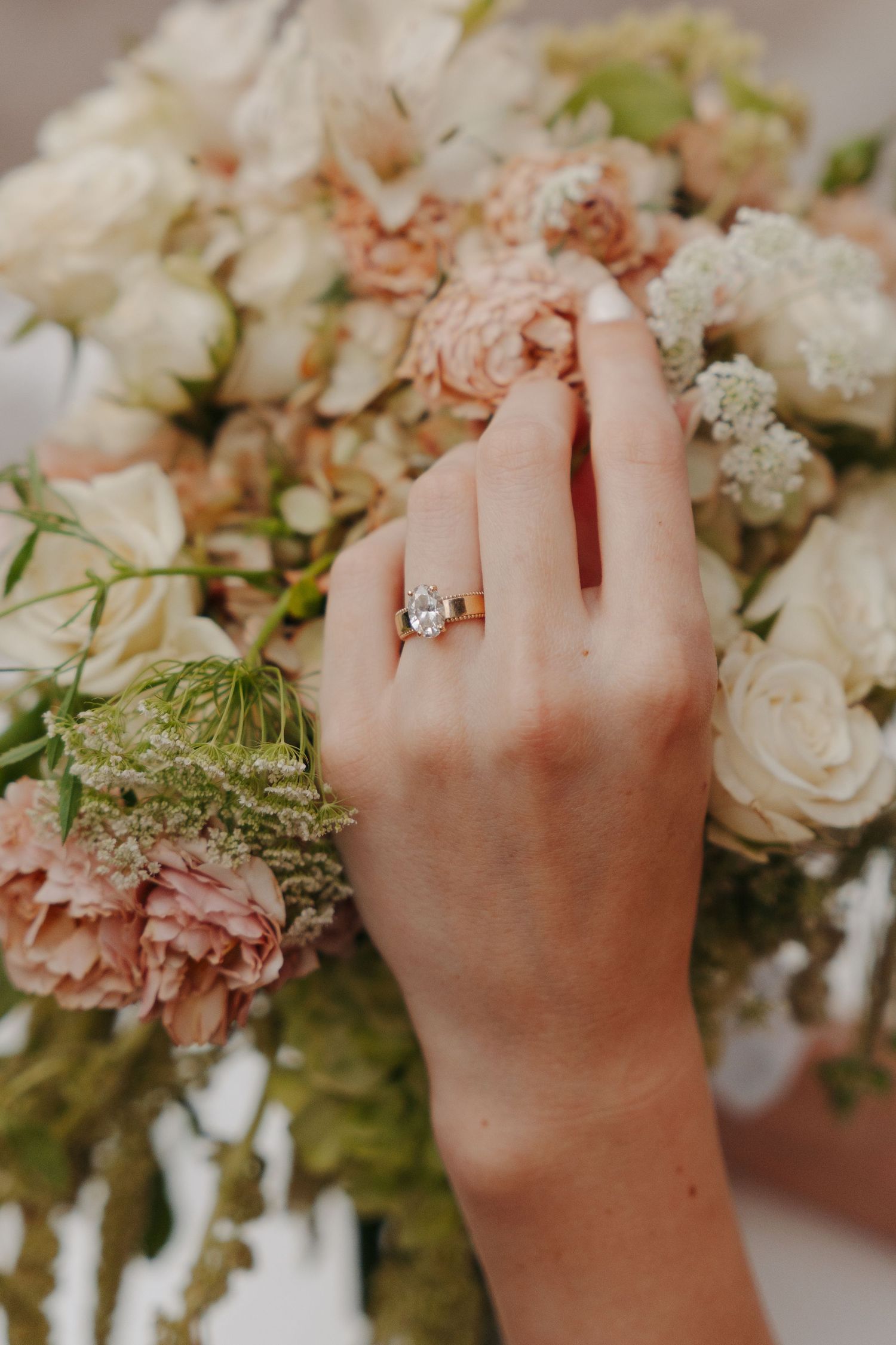 Close-up of hands wearing an engagement ring while arranging white and pink floral wedding bouquet decorations.