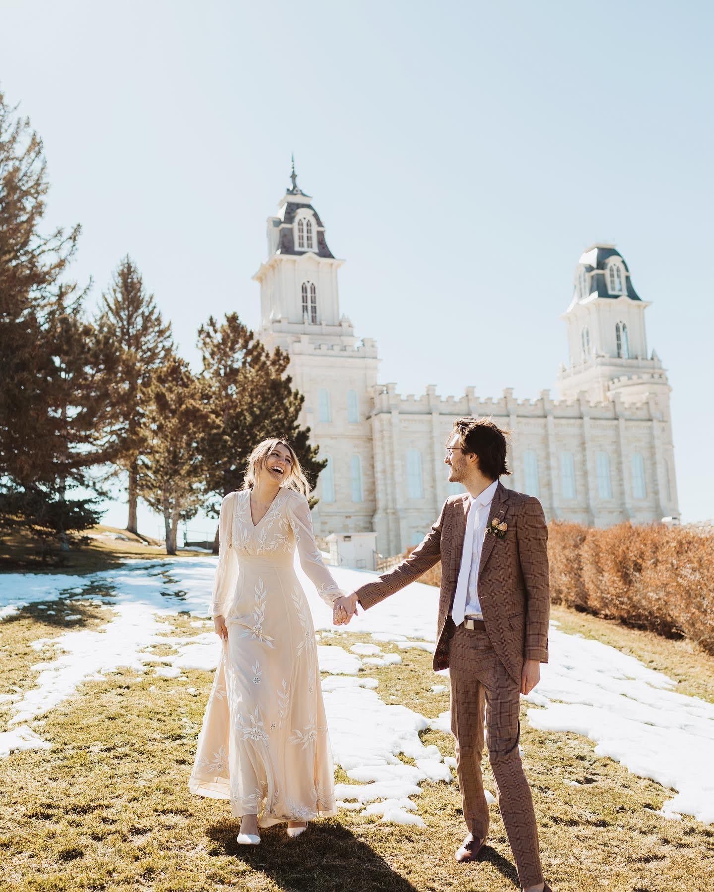 Wedding couple poses in front of white domed temple building on sunny winter day.
