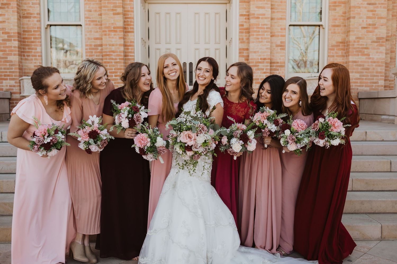 Wedding party photo featuring bridesmaids in coordinated pink and burgundy dresses.