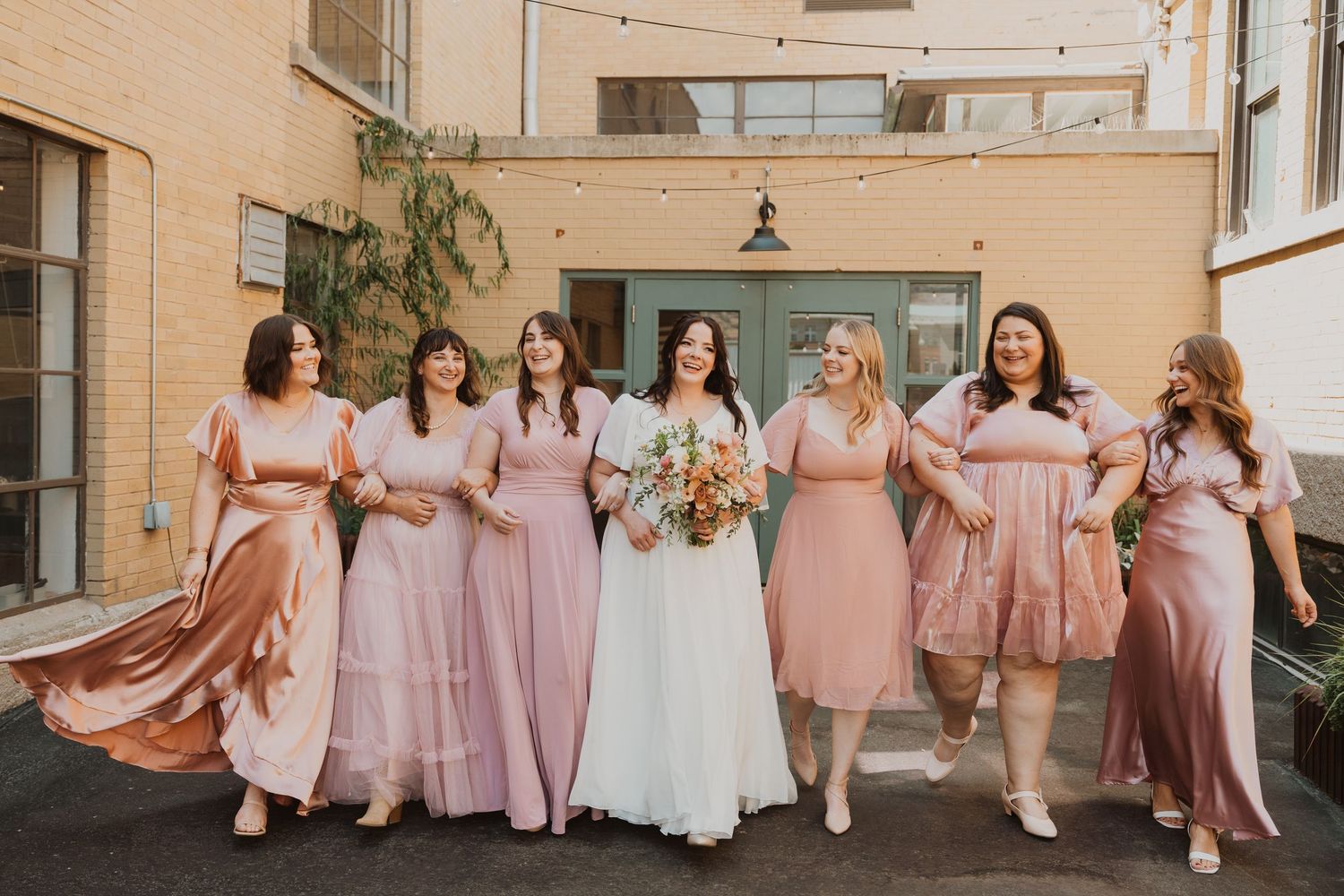 Utah Wedding party in pink dresses posing together in urban courtyard setting.