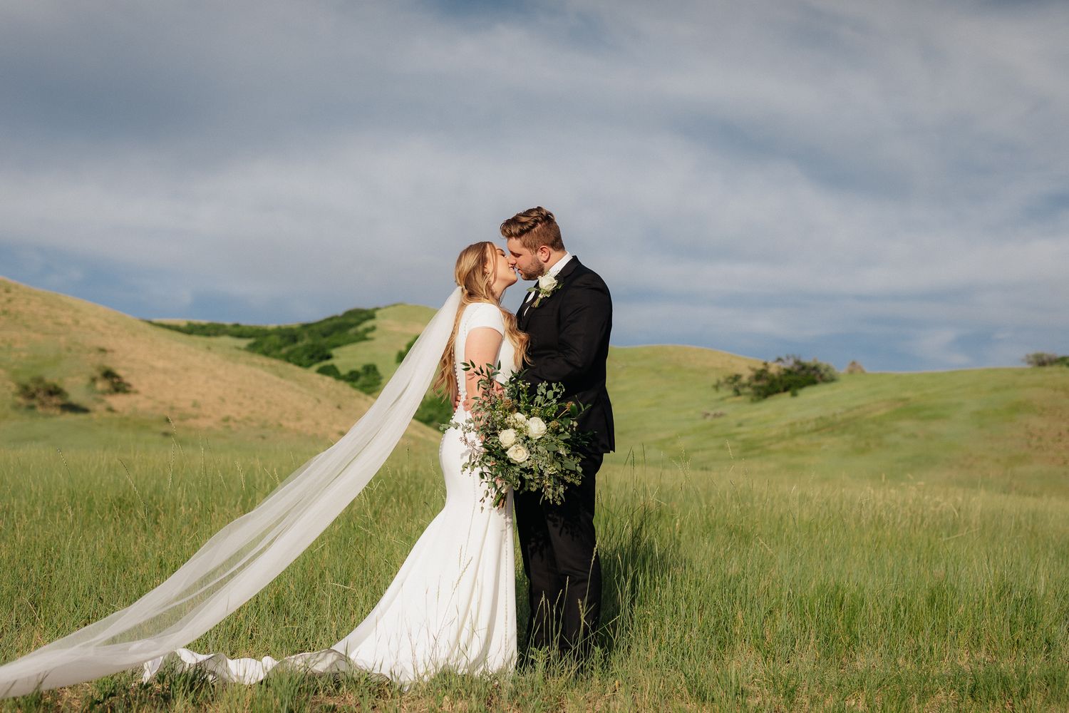 A couple shares an intimate moment on rolling green hills with a winding country road in the background in Tunnel Springs SLC Utah.