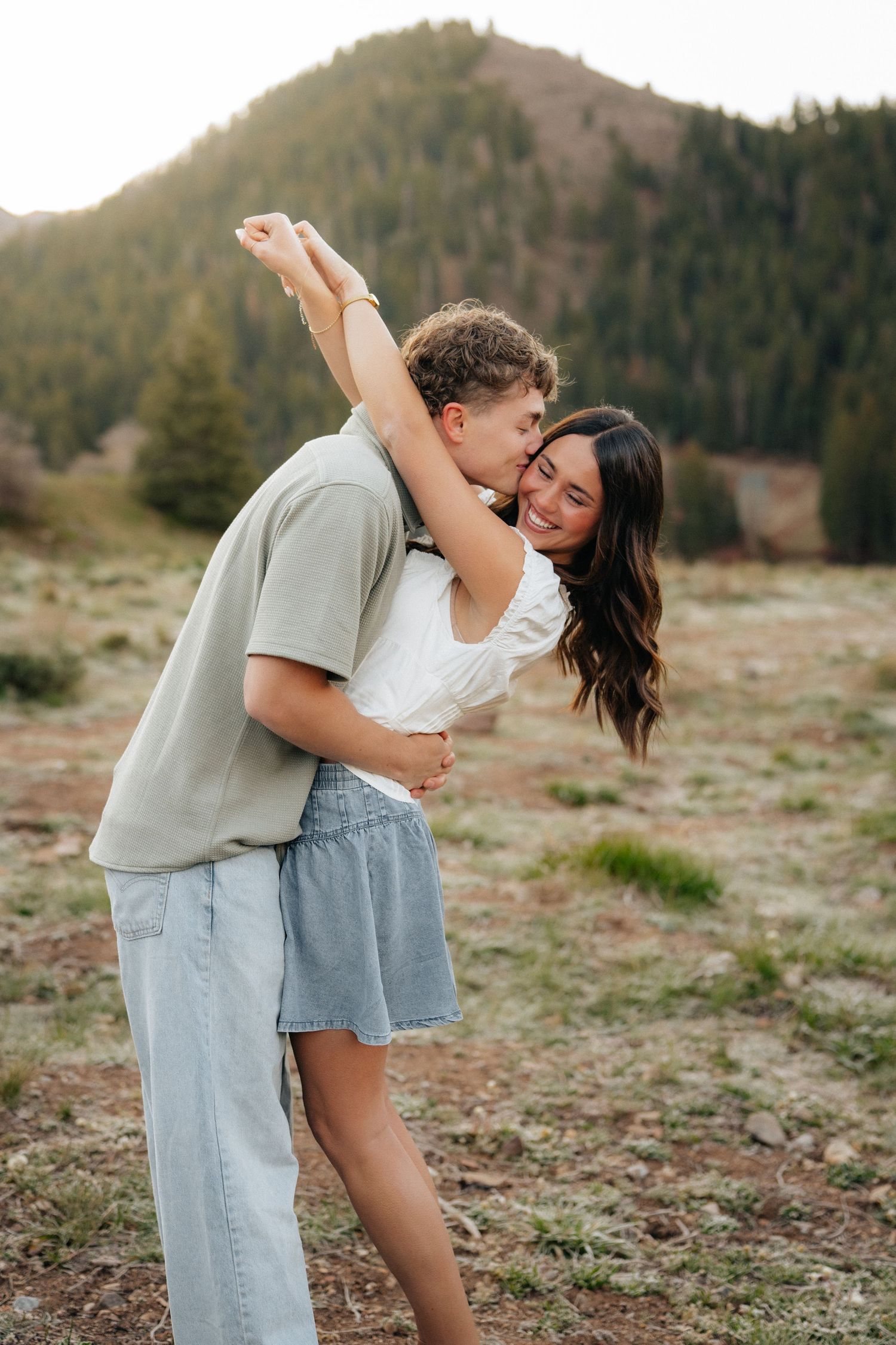 Happy couple embracing and laughing in mountain meadow during golden hour engagement photos.