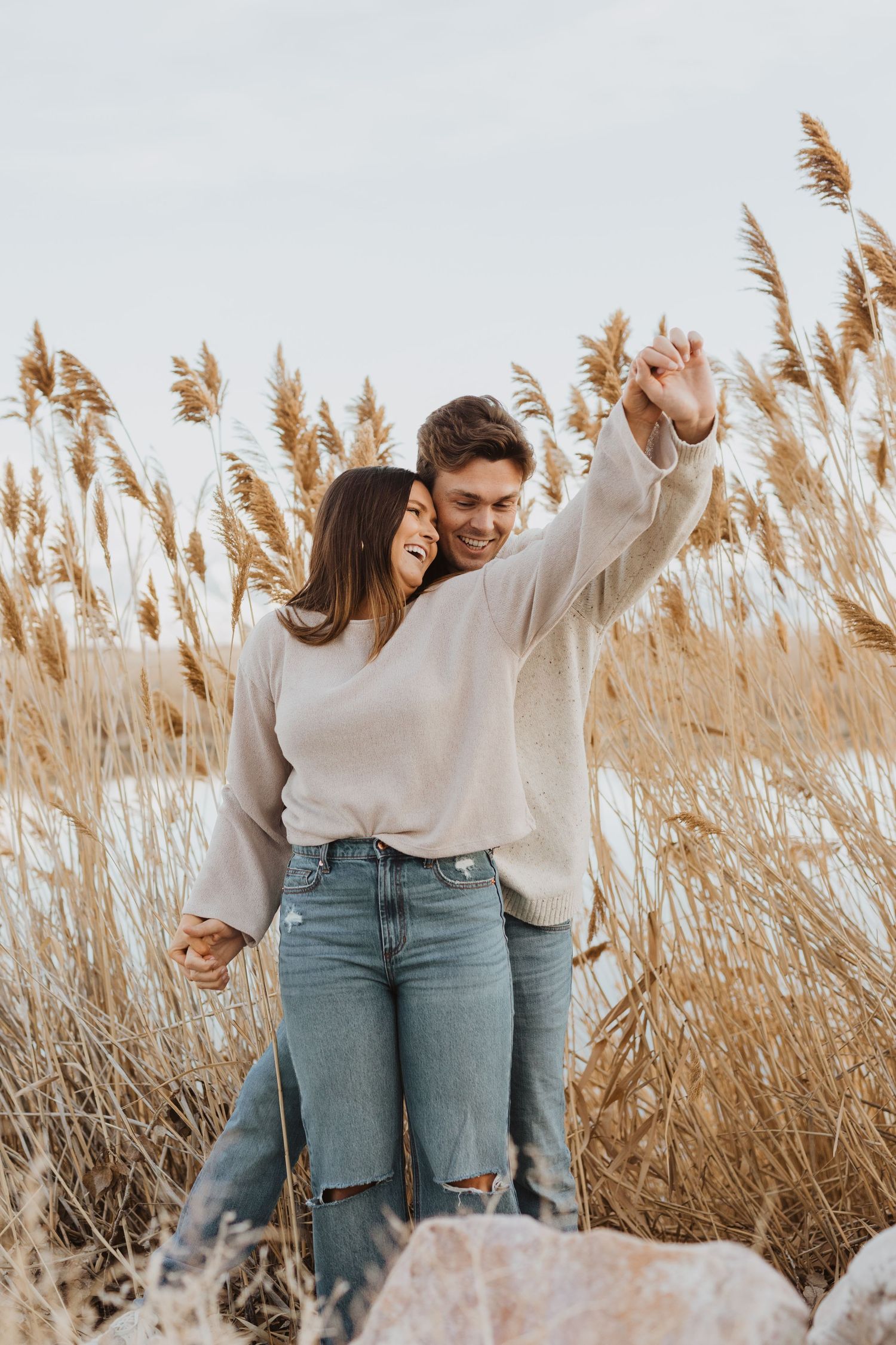 A joyful couple embraces among tall golden pampas grass on a sunny day.
