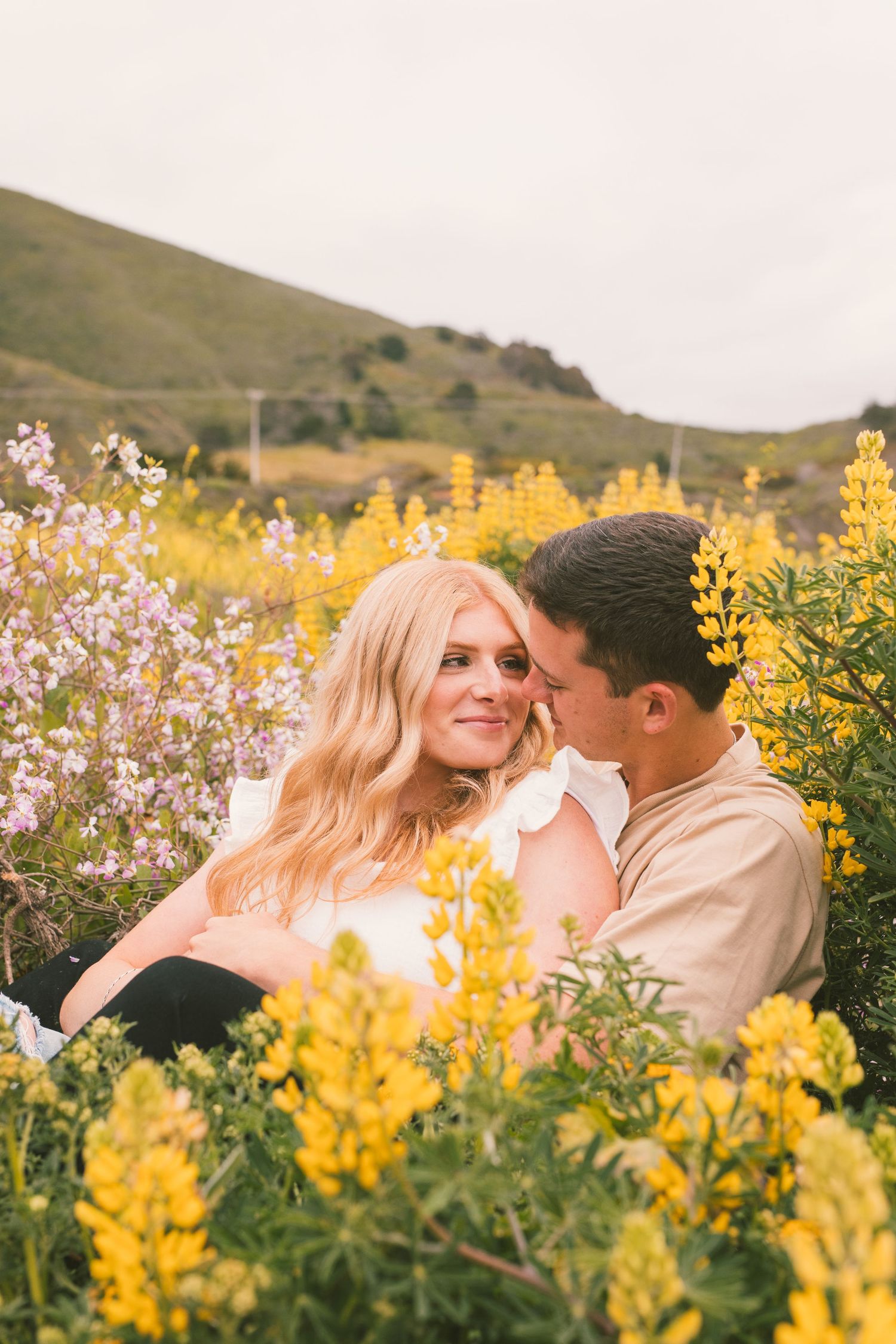 Couple sharing tender moments among blooming yellow and purple wildflowers on hillside.