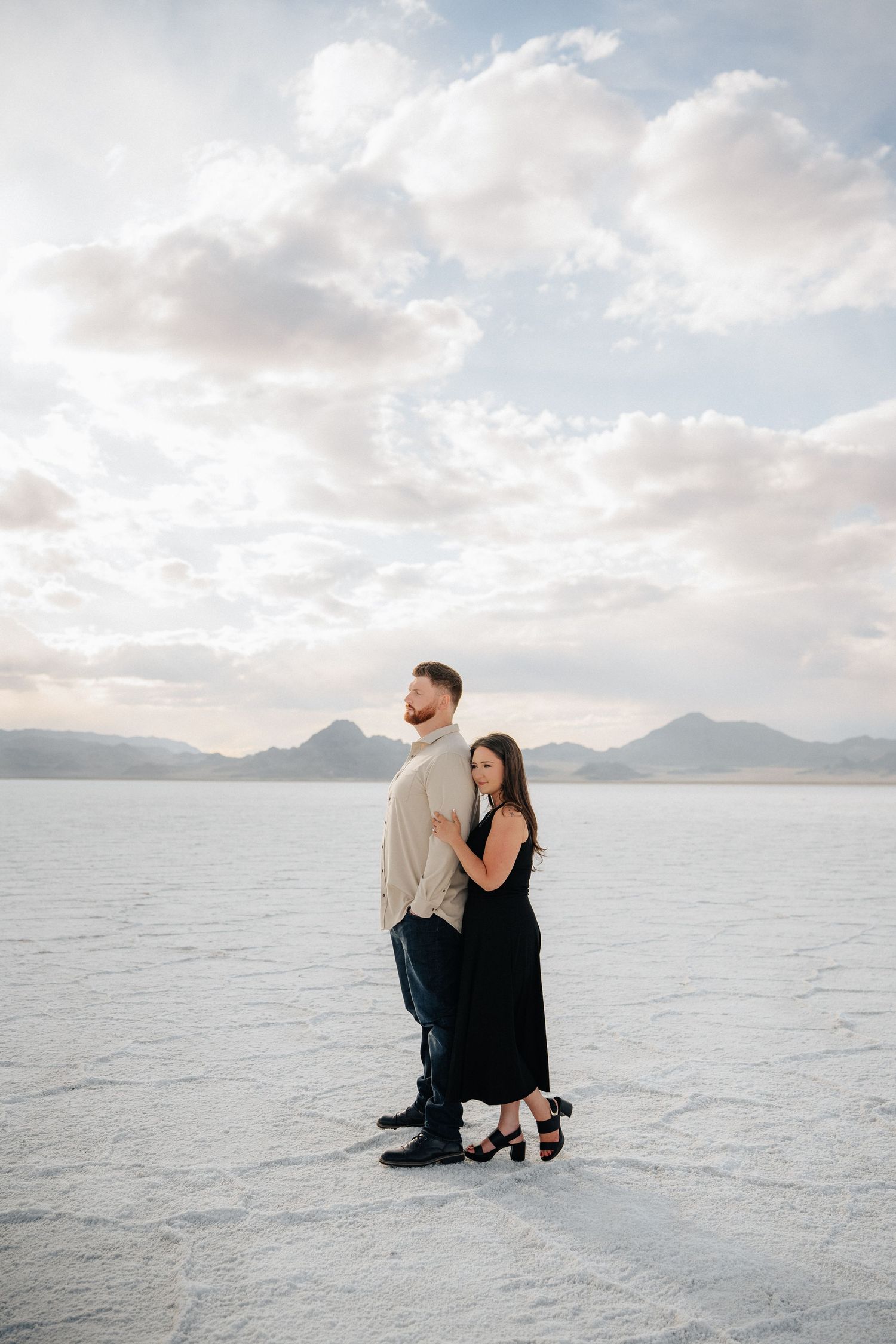 Couple embracing on the Bonneville Salt Flats with mountains and dramatic clouds in the background.