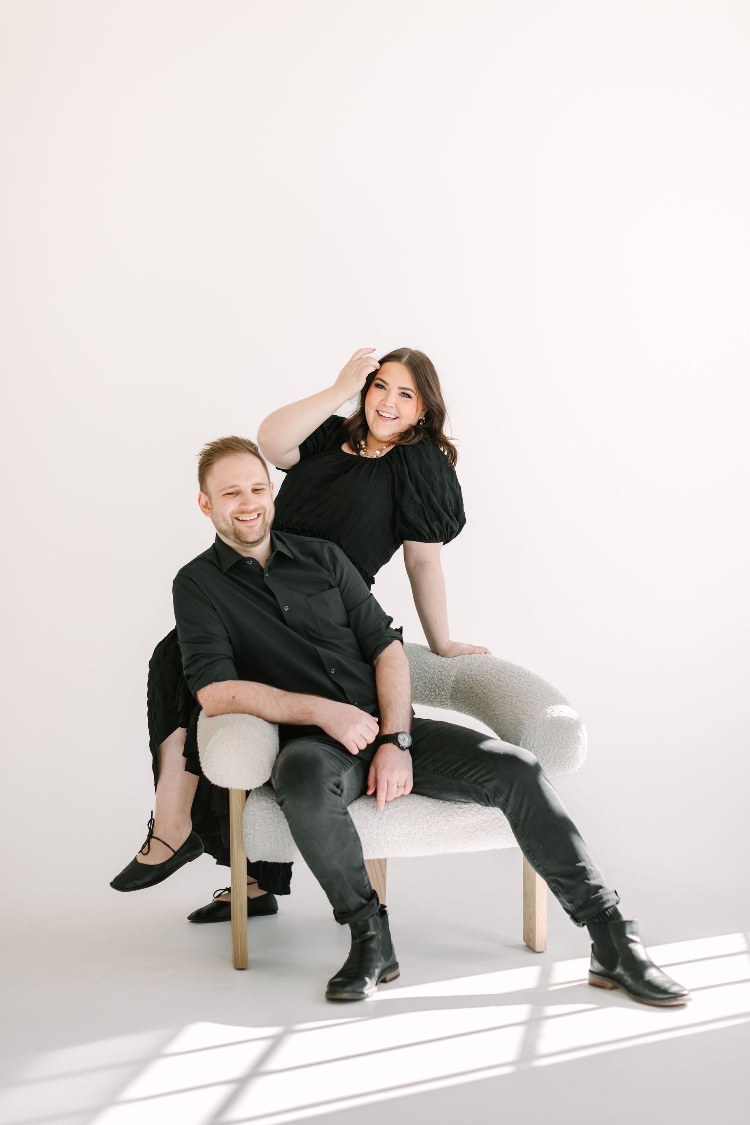 Two people, a man and a woman, are sitting on a chair and posing for a portrait against a white background.