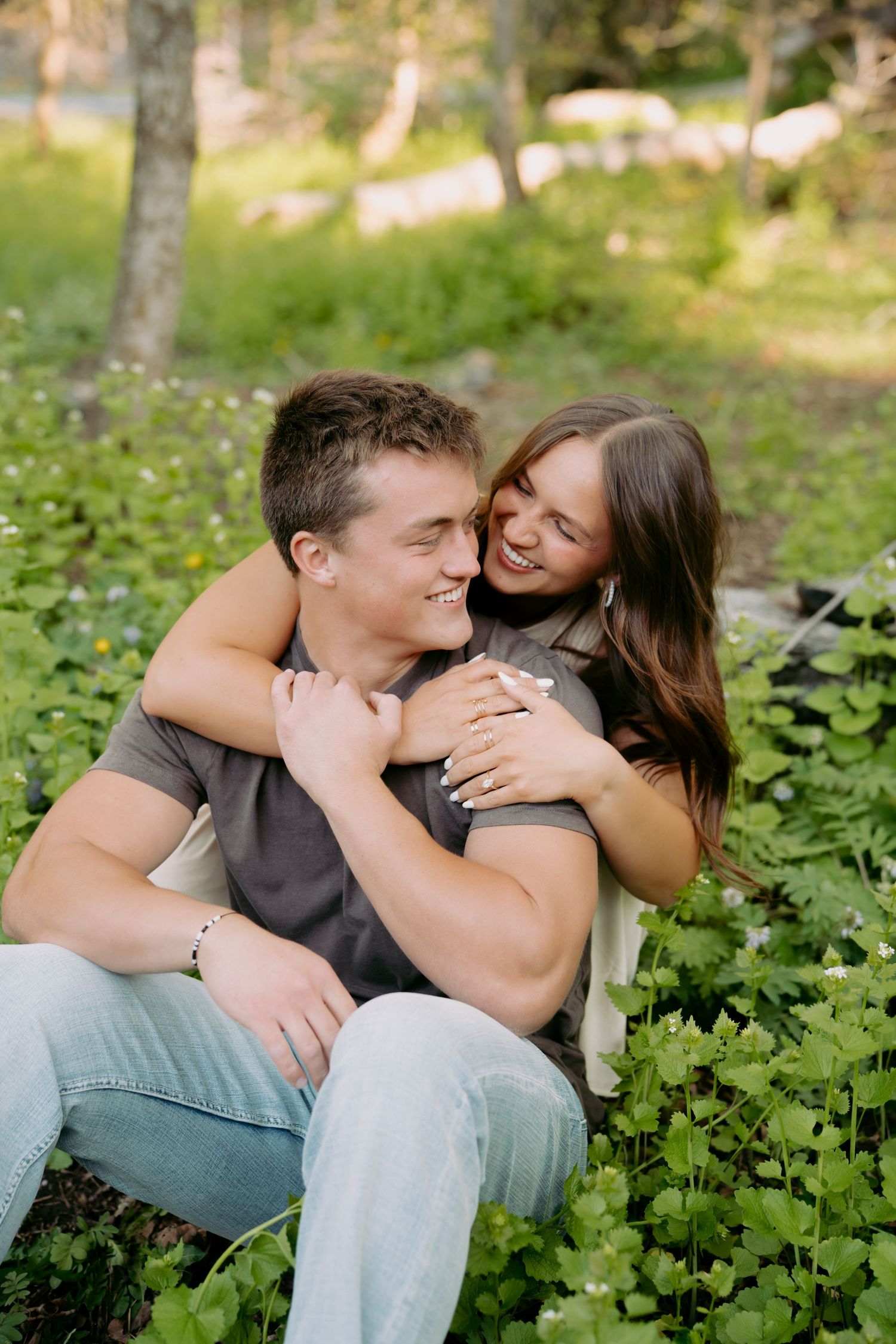 A happy couple embraces in a lush green meadow, smiling and sharing a romantic moment outdoors.