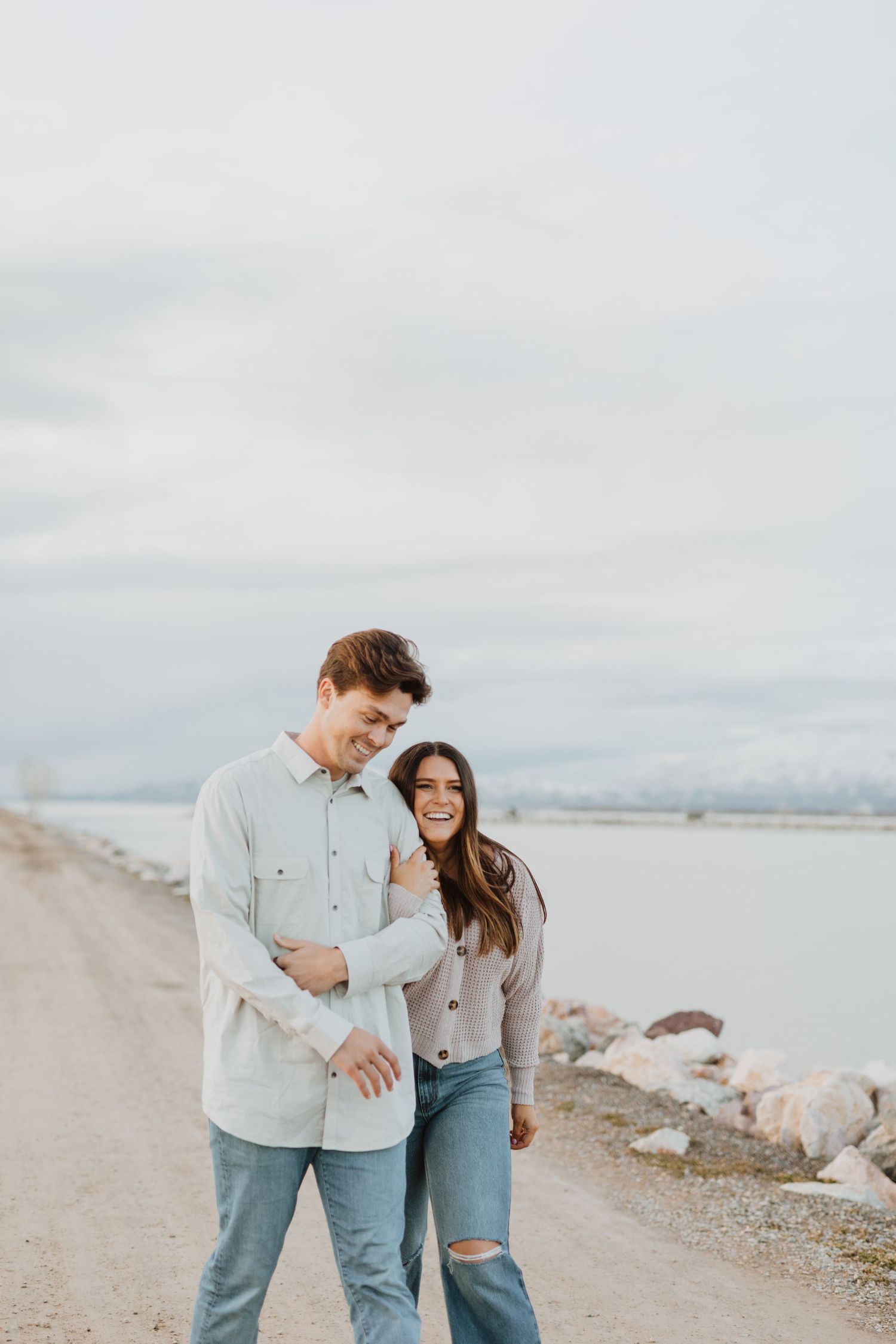 A casual couple shares a laugh while walking along a rocky coastline.