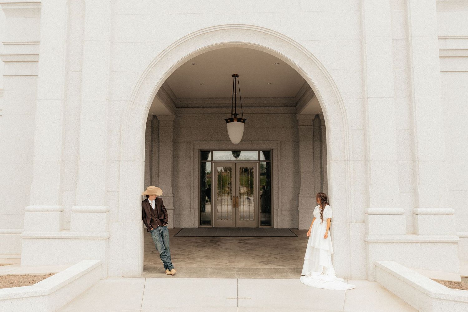 Bride and groom share a romantic first look moment at a grand white arched building entrance.