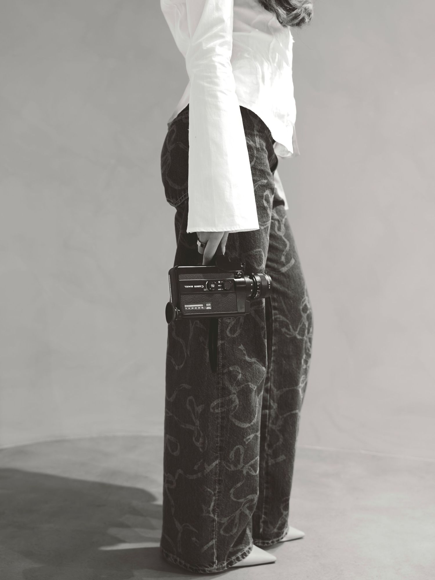 Black and white photo of a model wearing wide-leg camo jeans, white top, and a small belt bag accessory.
