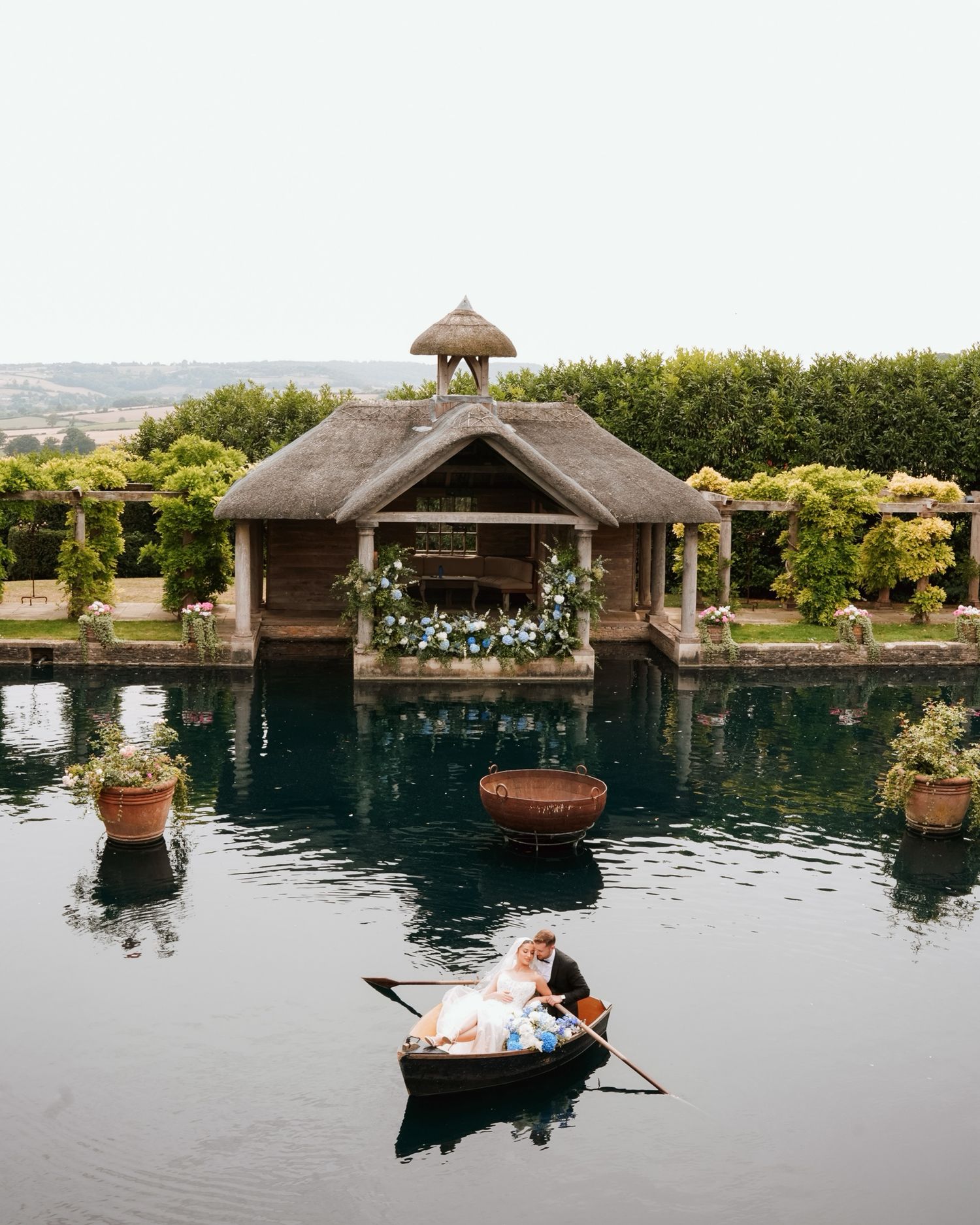 Romantic waterfront wedding venue with thatched gazebos reflected in still pool at sunset.