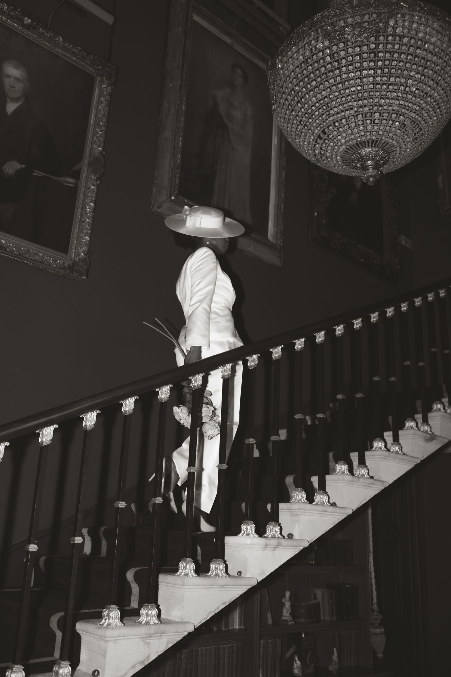 Dramatic black and white photo of wedding dress on grand staircase with crystal chandelier.