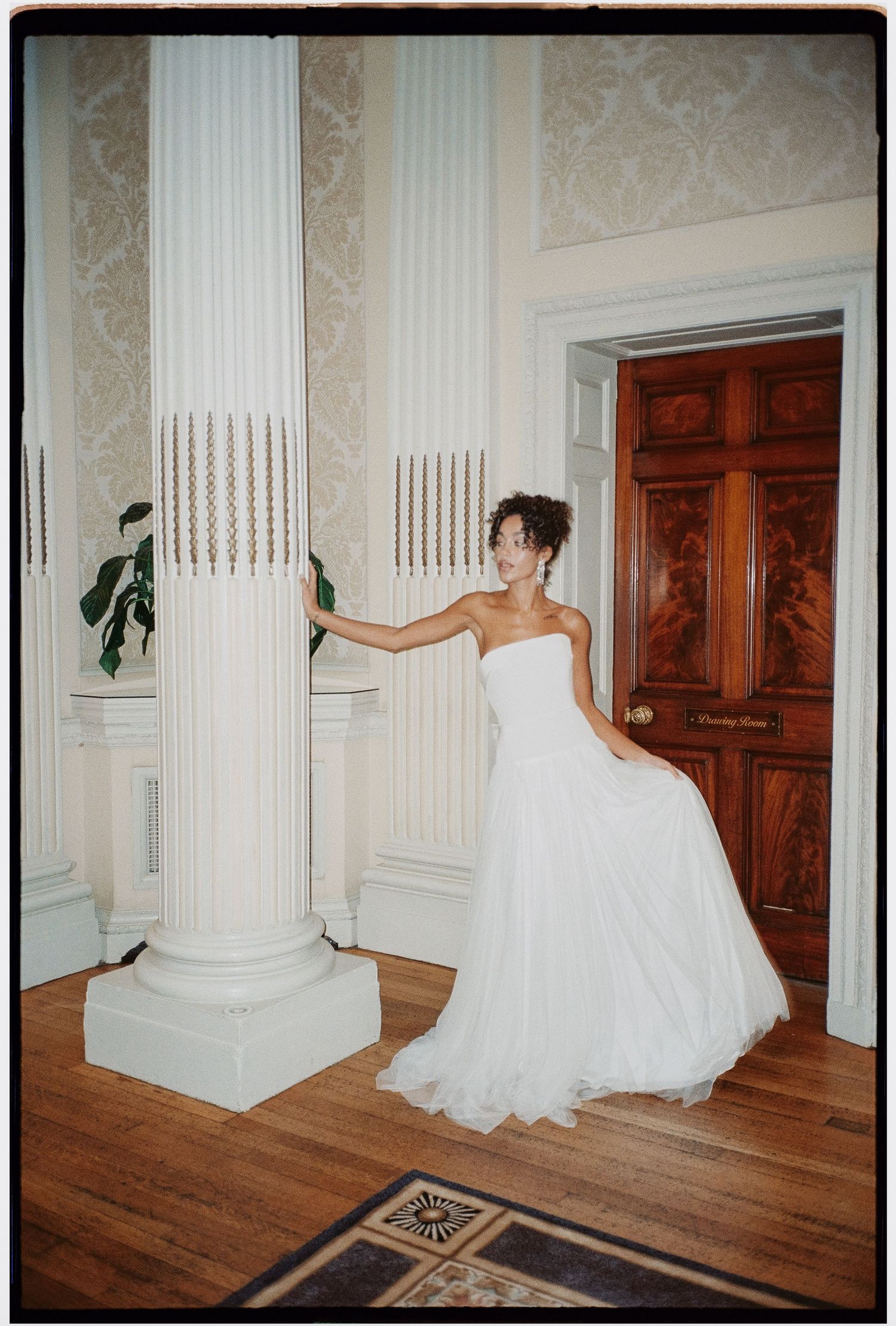 Artistic sequence of a white wedding dress flowing across a grand room with white columns and wooden floors.