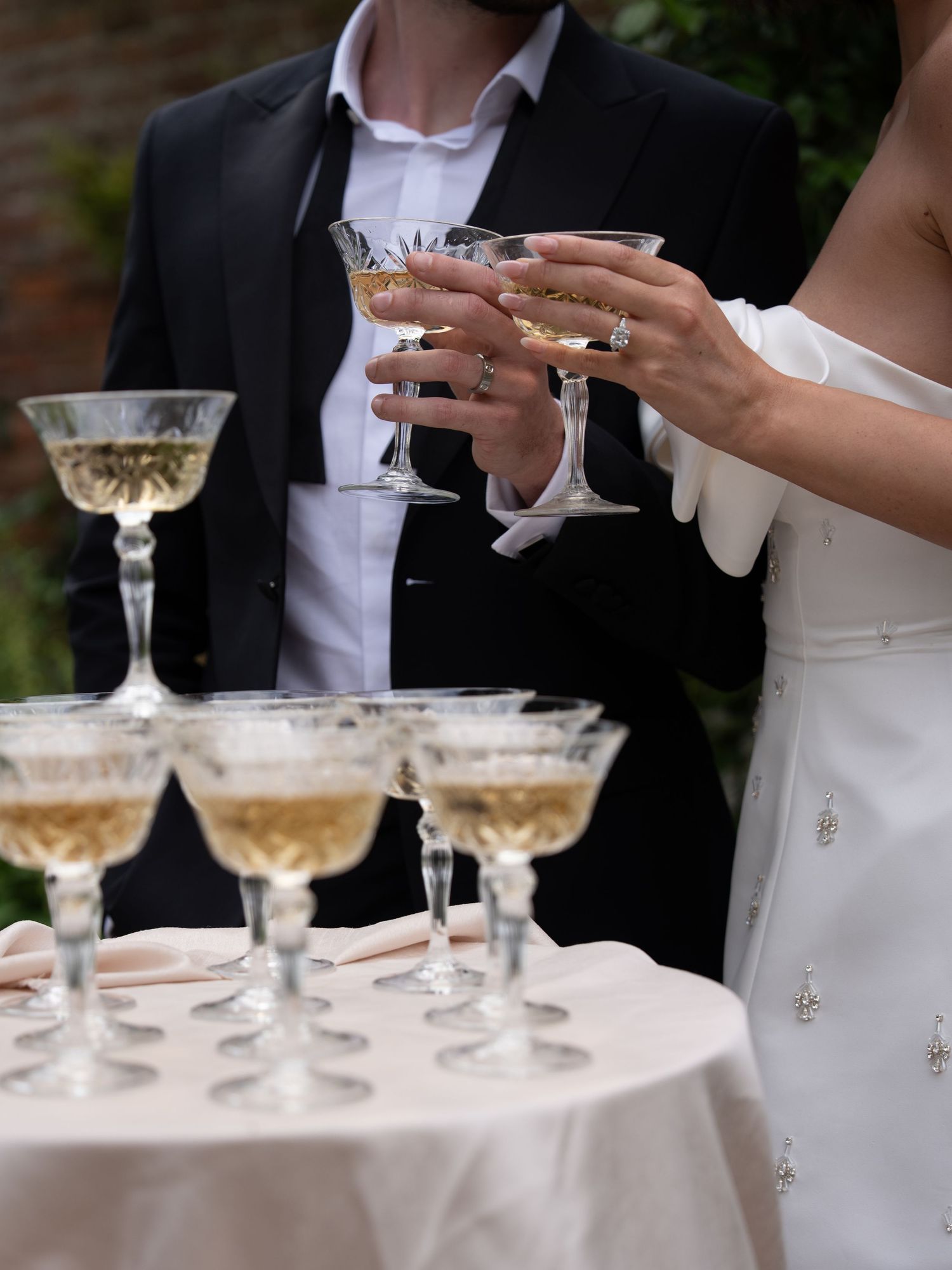 Bride and groom toasting with champagne coupe glasses at a wedding reception table filled with sparkling drinks.
