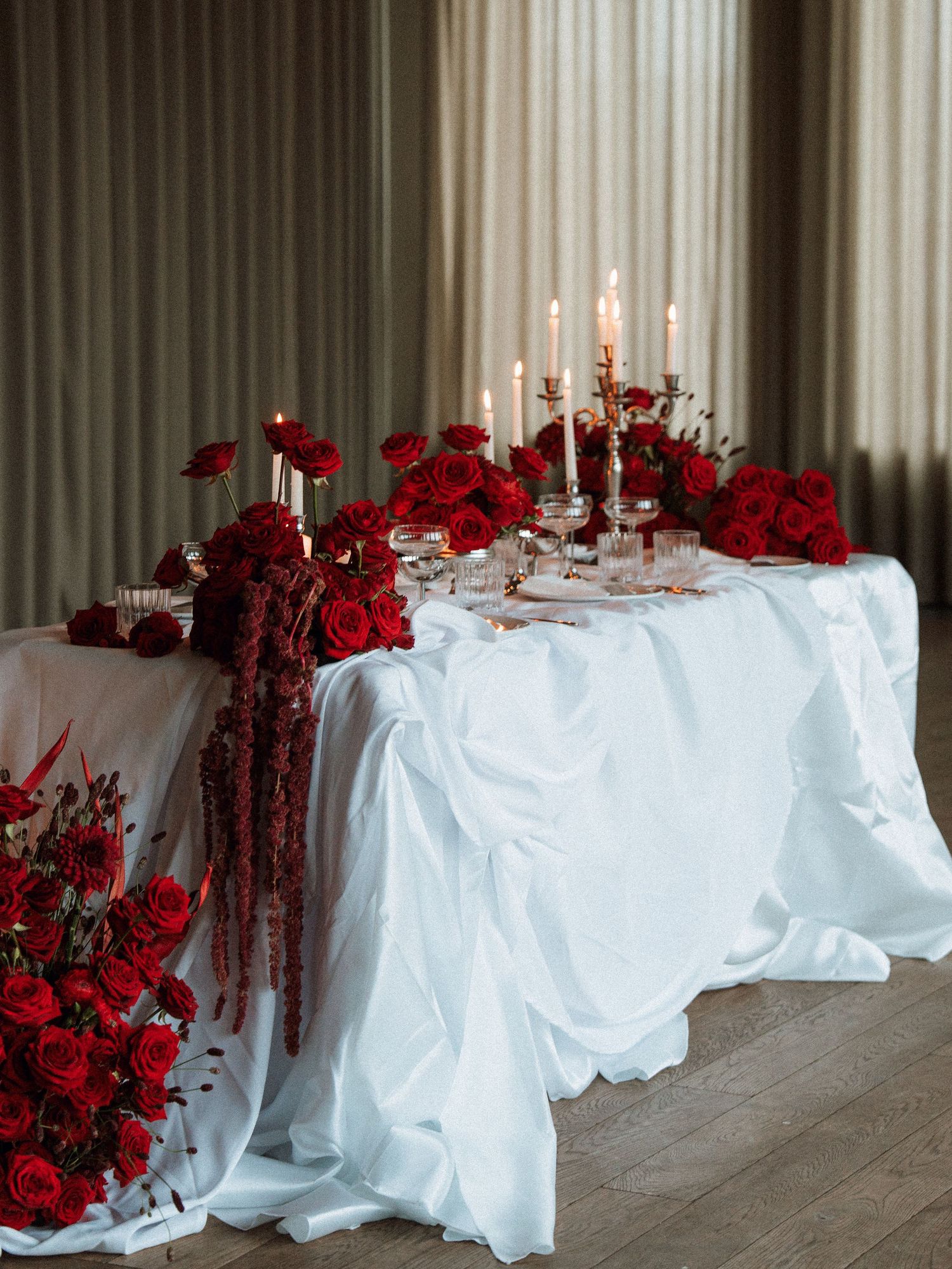Elegant wedding reception tables with white linens and dramatic red floral centerpieces alongside tall white candles.