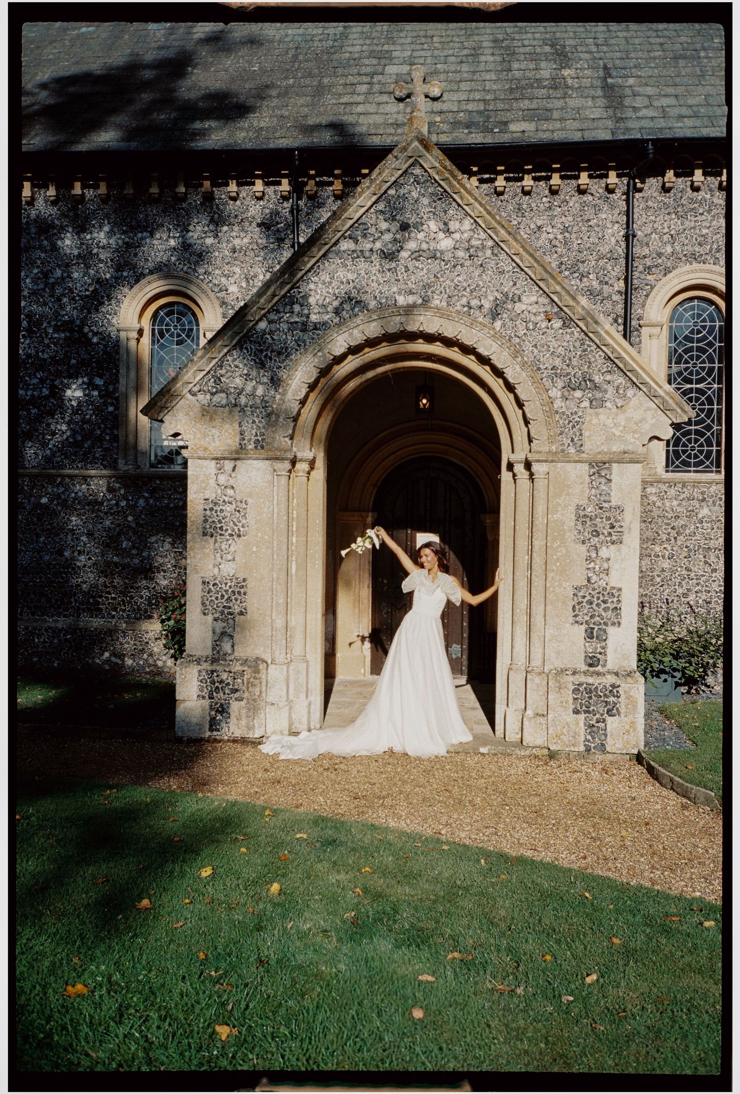 Bride in flowing white dress posing at gothic church entrance.