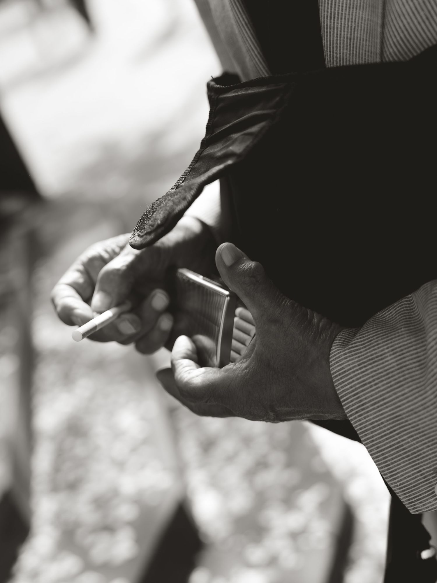 Black and white photo of a man's hands holding a cigarette and a lighter outdoors.