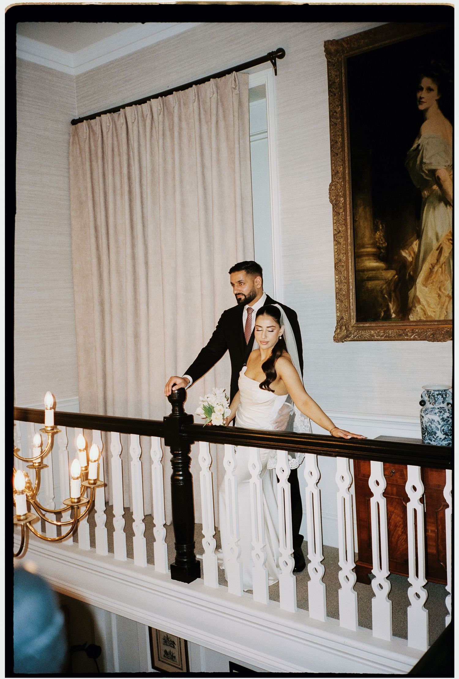 A couple shares a playful moment along an elegant white railing in a classic interior setting.