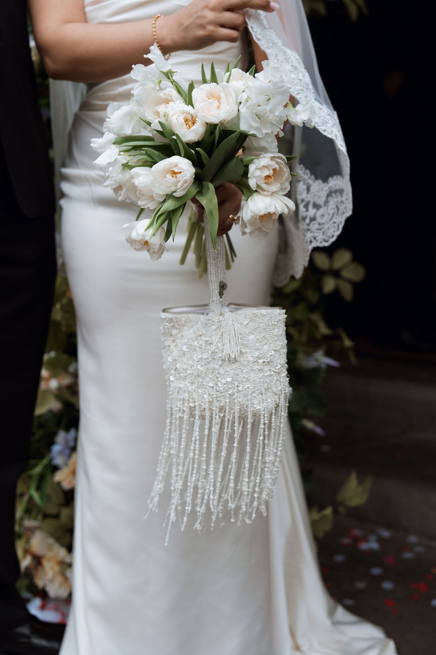 Close-up view of an elegant white wedding dress with beaded fringe detail and delicate floral bouquet accents.