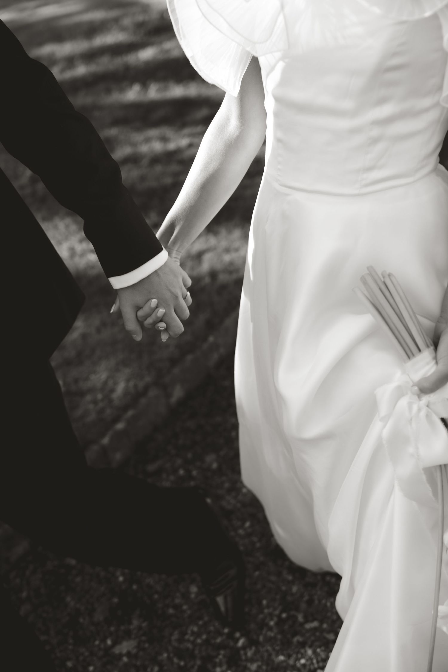 Black and white detail shot of elegant wedding dress and hands against dark background.