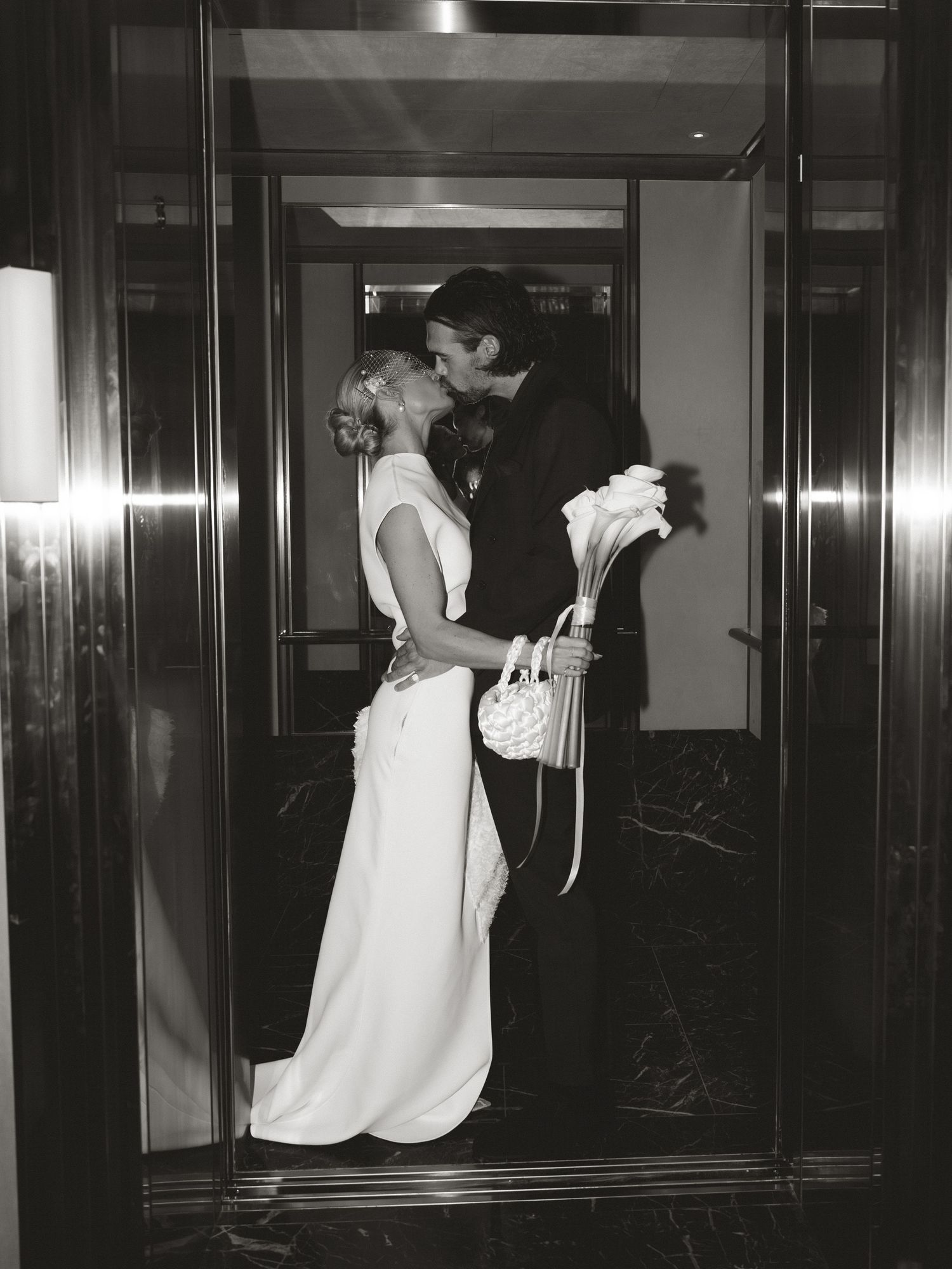 Black and white photo of a bride and groom sharing a kiss in a doorway, bride holding a bouquet.