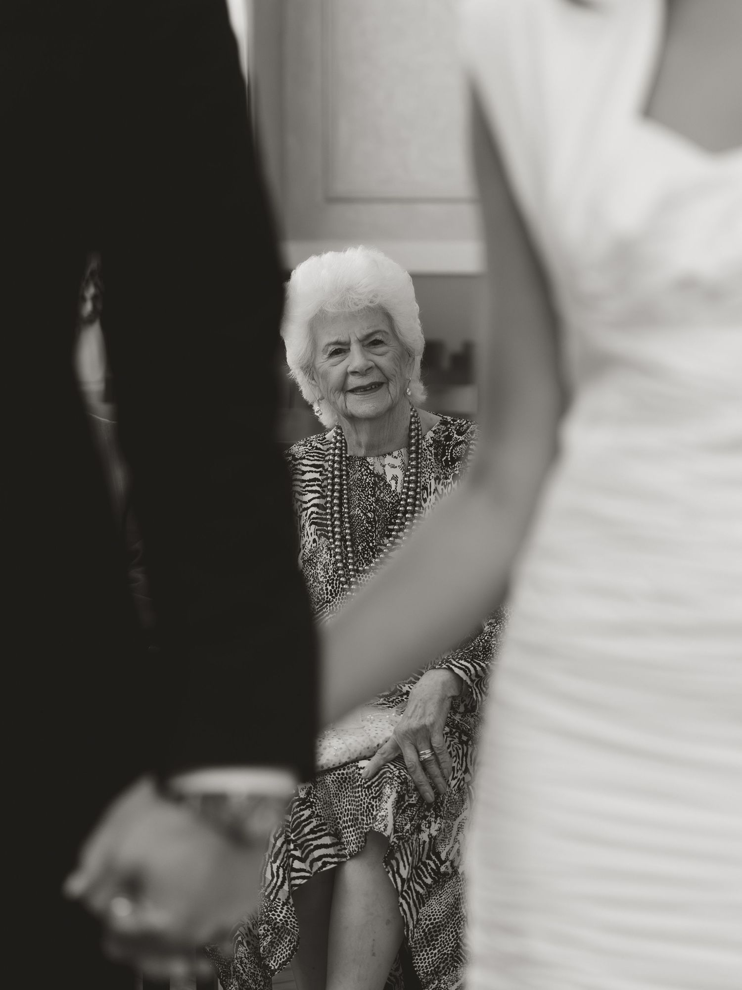 Elderly woman smiling warmly at a wedding ceremony, captured in elegant black and white photography.