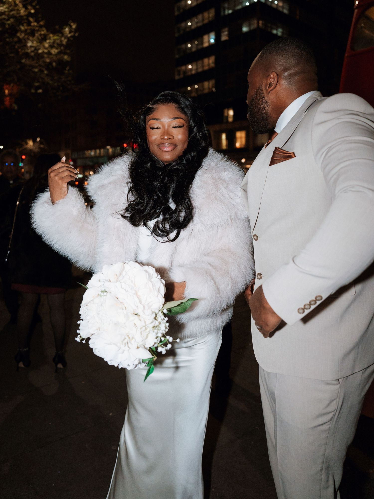 A couple in white and cream formal attire dances together at an outdoor evening celebration.