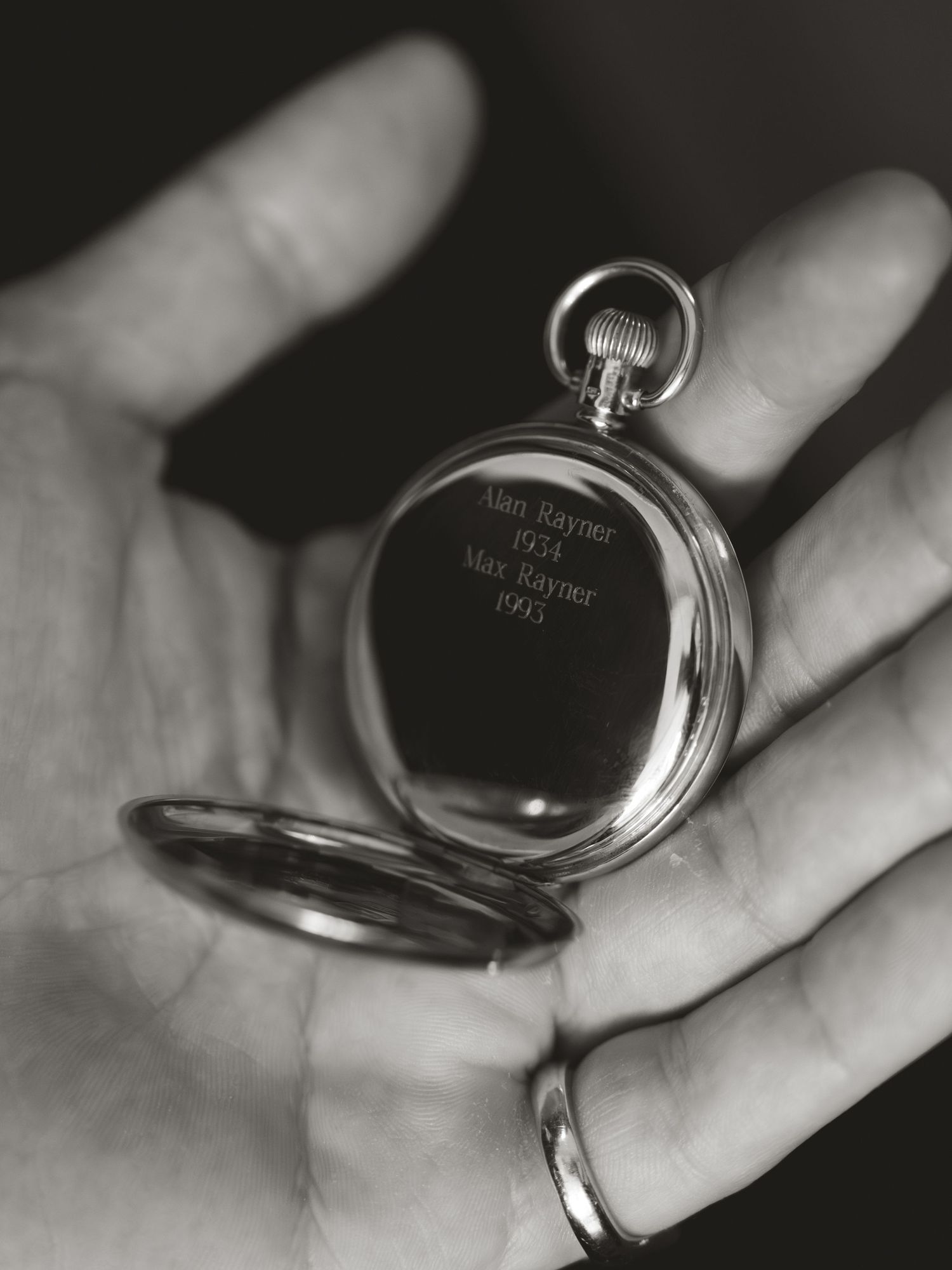 Black and white photo of a hand holding an engraved silver pocket watch with names Alan Rayner 1934 and Max Rayner 1970.