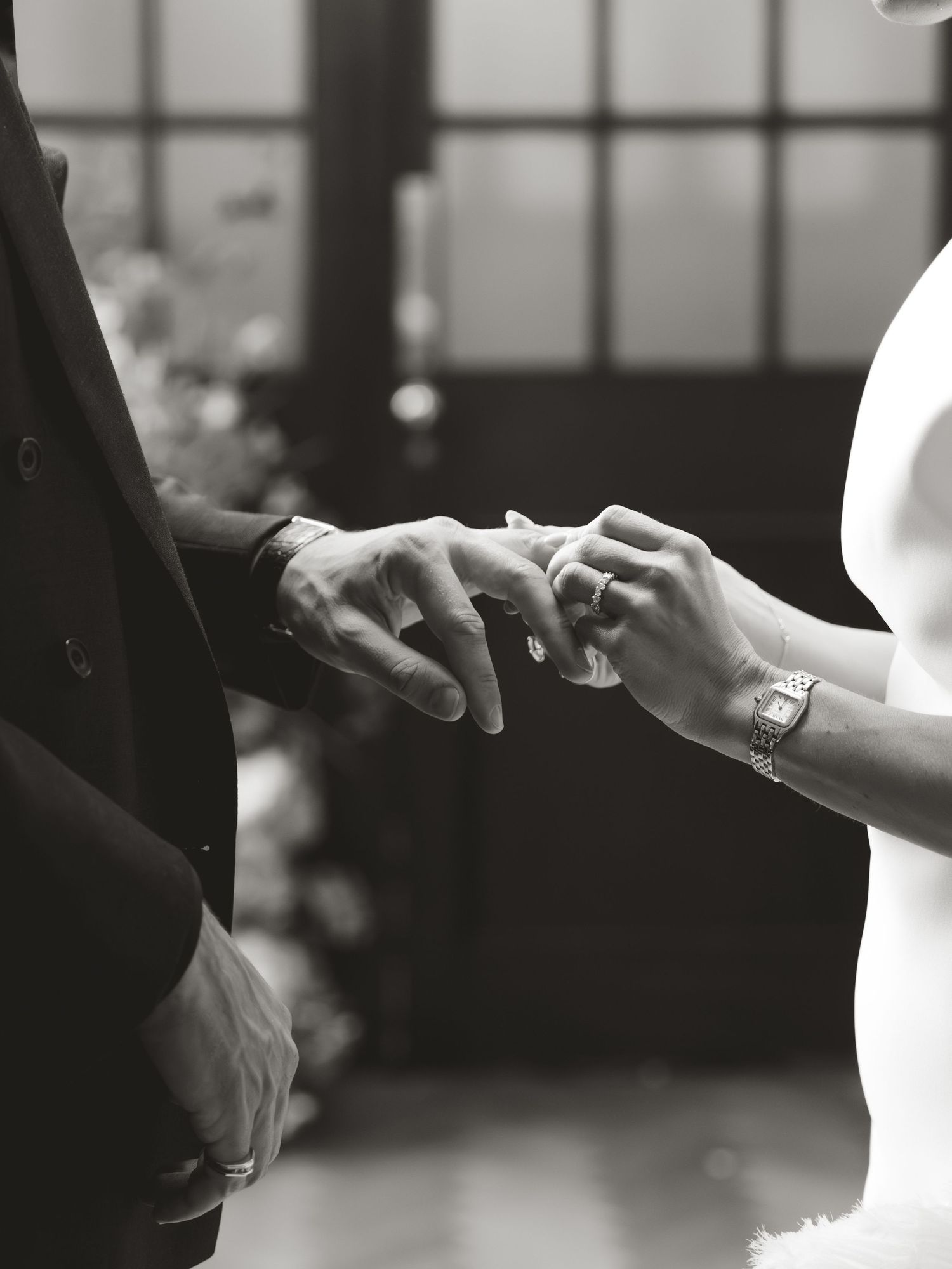 Black and white photo of a couple exchanging wedding rings during a ceremony, bride placing ring on groom's finger.