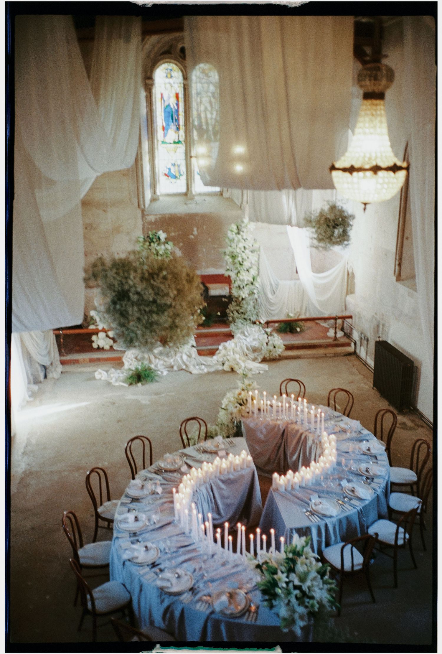 An elegant wedding reception setup with curved tables and white draping in a historic chapel.