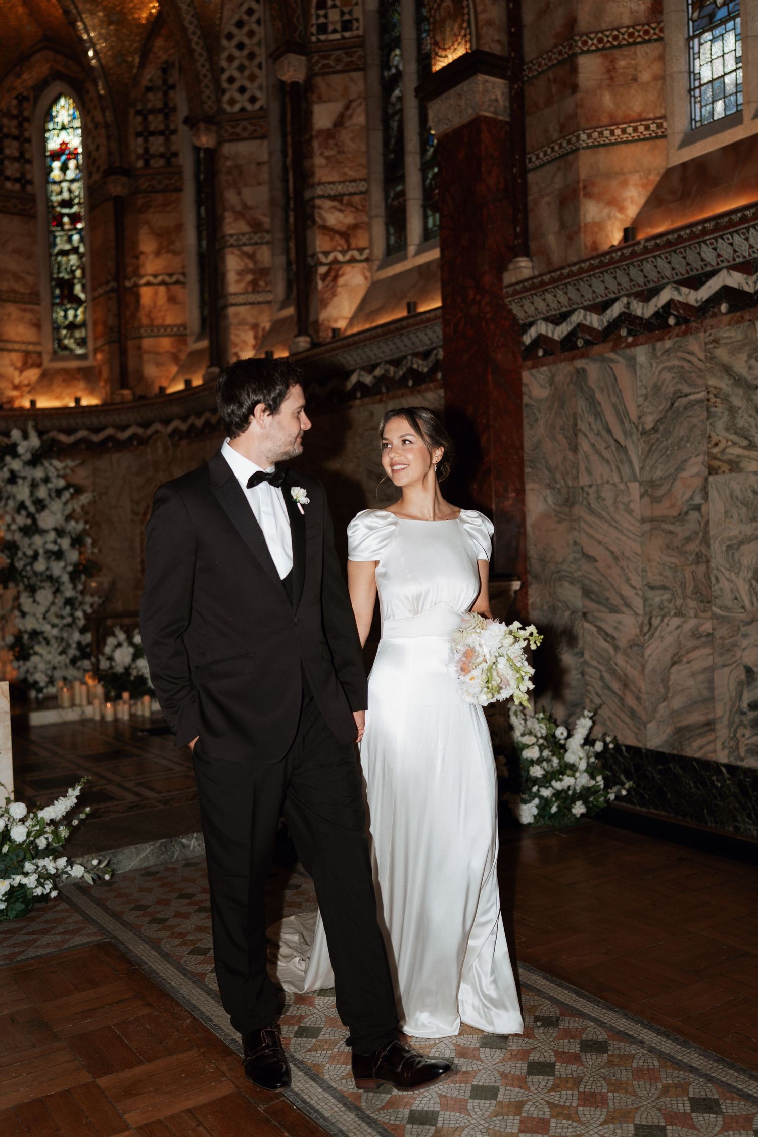 A wedding couple shares intimate moments in an ornate church interior with stained glass windows.