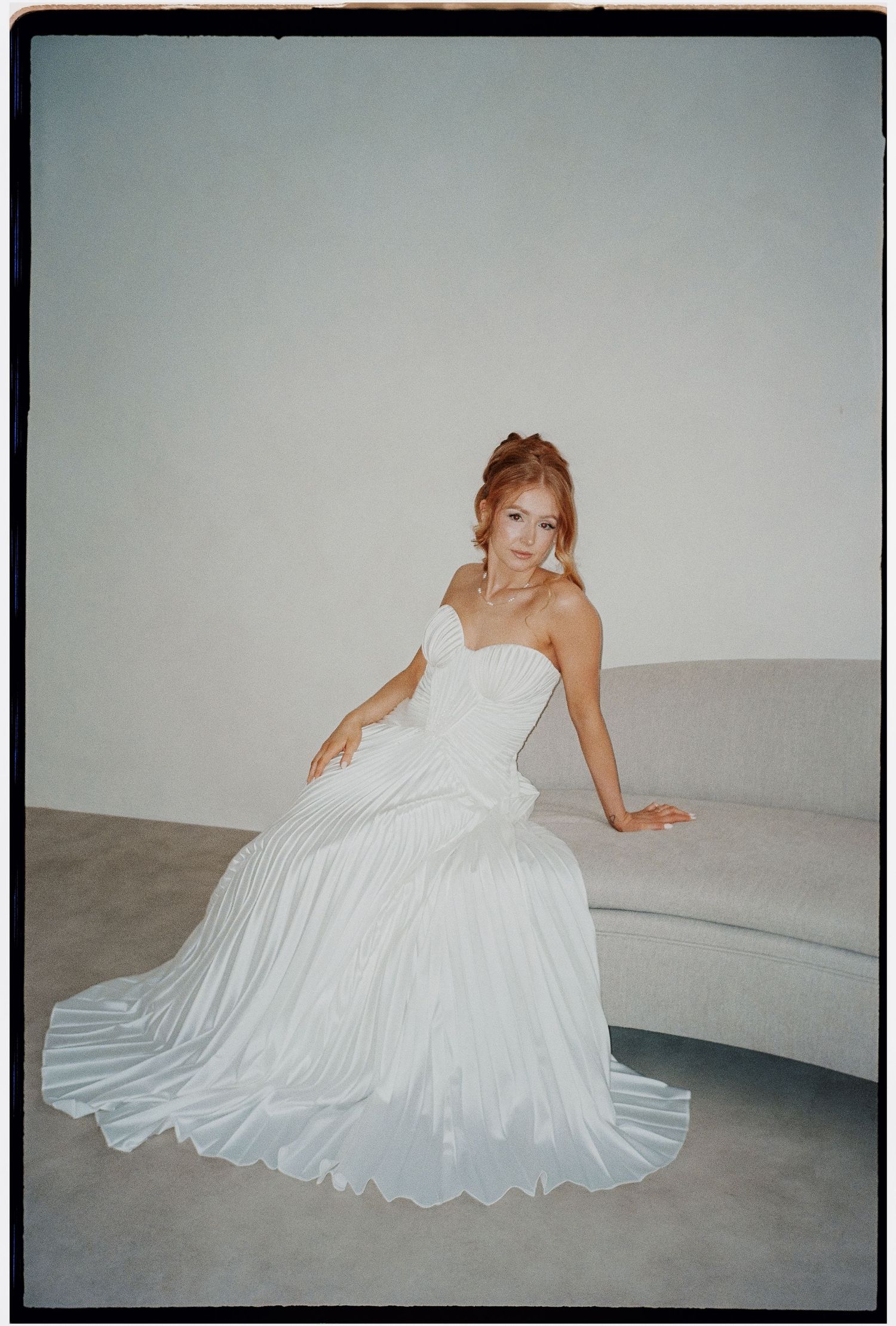 A woman in a white strapless wedding gown poses gracefully on a curved bench.