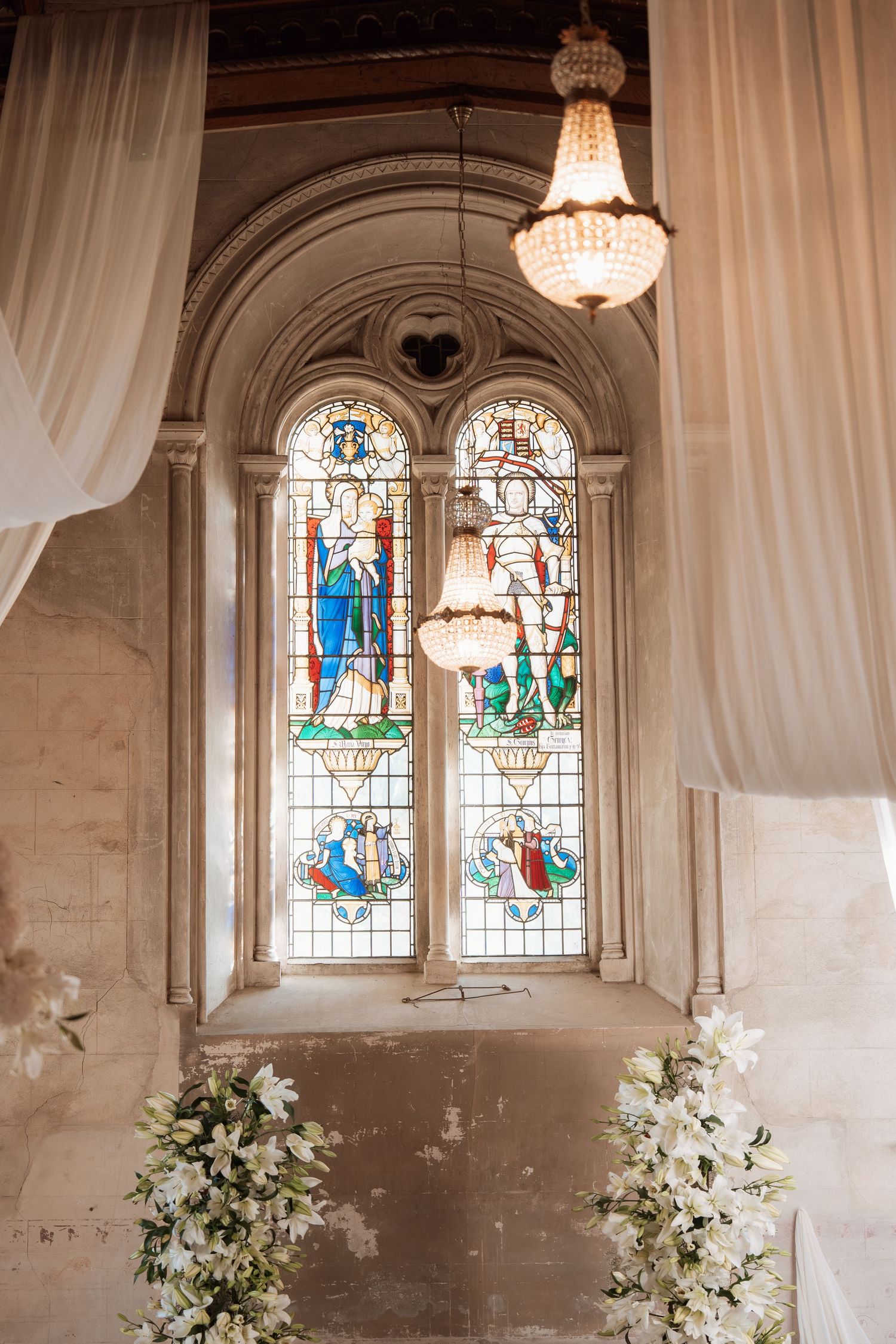 Elegant church interior with stained glass windows, crystal chandeliers, and white floral arrangements.