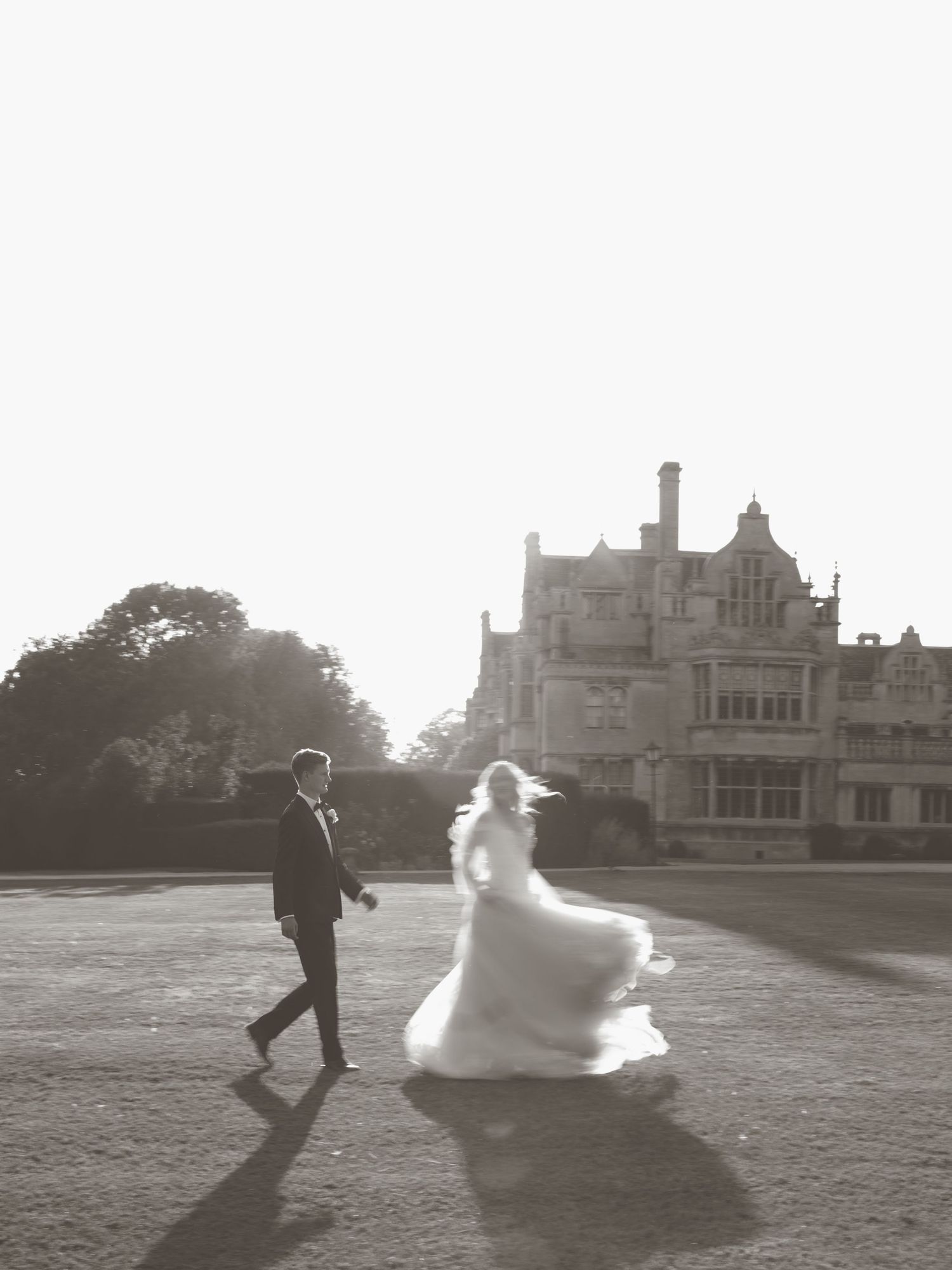 Black and white wedding photos showing couple running playfully across a grand estate lawn.