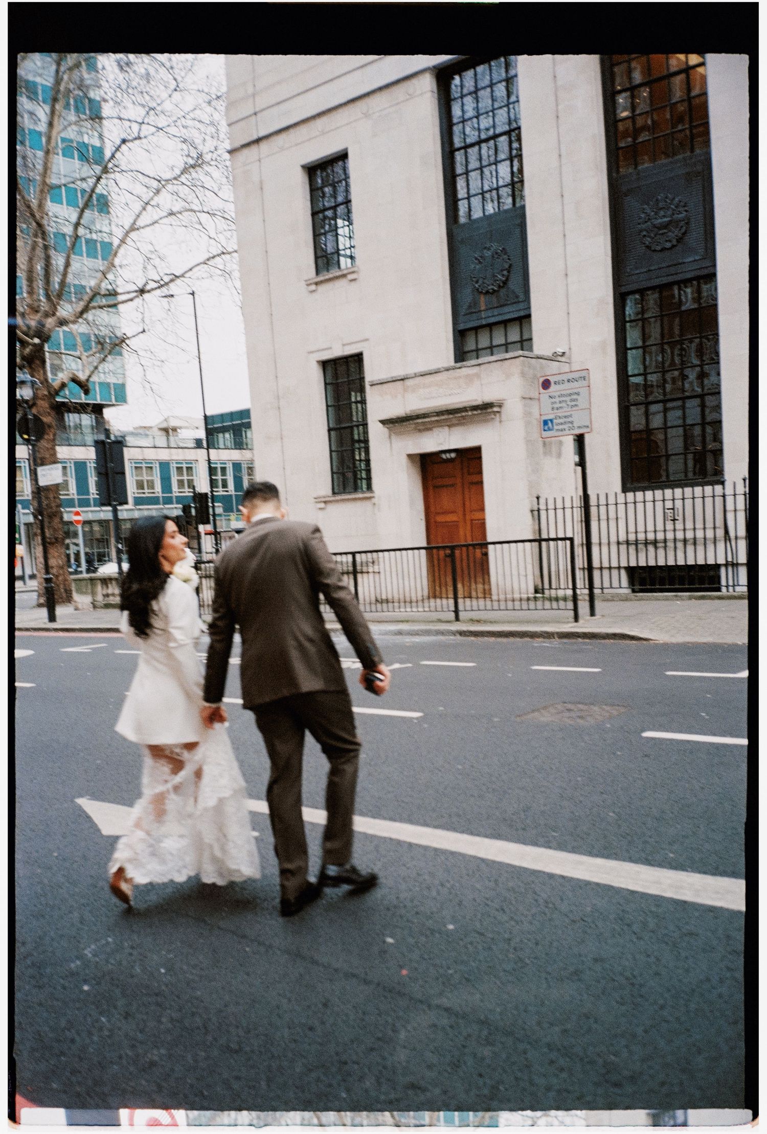 A couple walking hand in hand across a city street near a historic building.