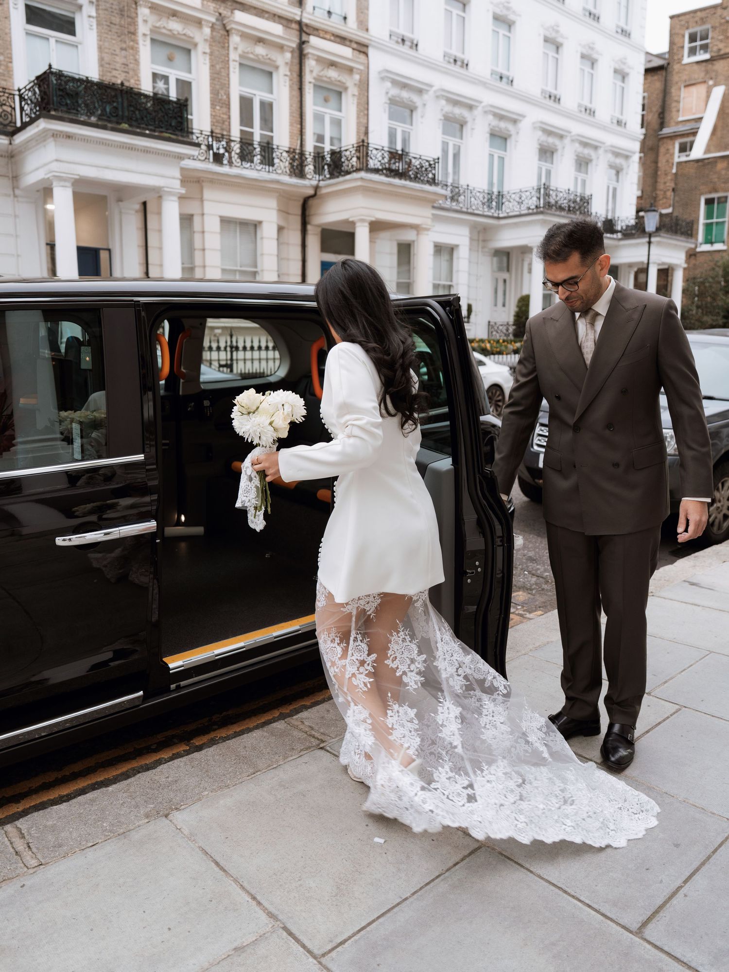 Wedding party entering luxury vehicles outside an elegant white townhouse.