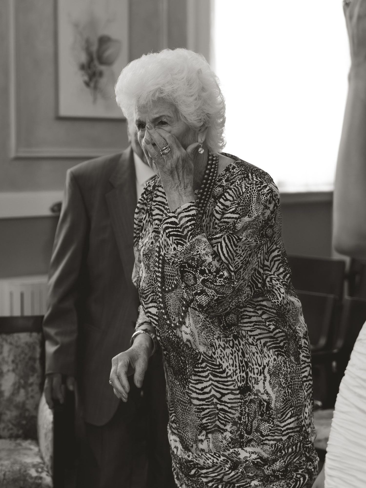 Elderly woman in zebra print dress laughing at indoor gathering, black and white photo.