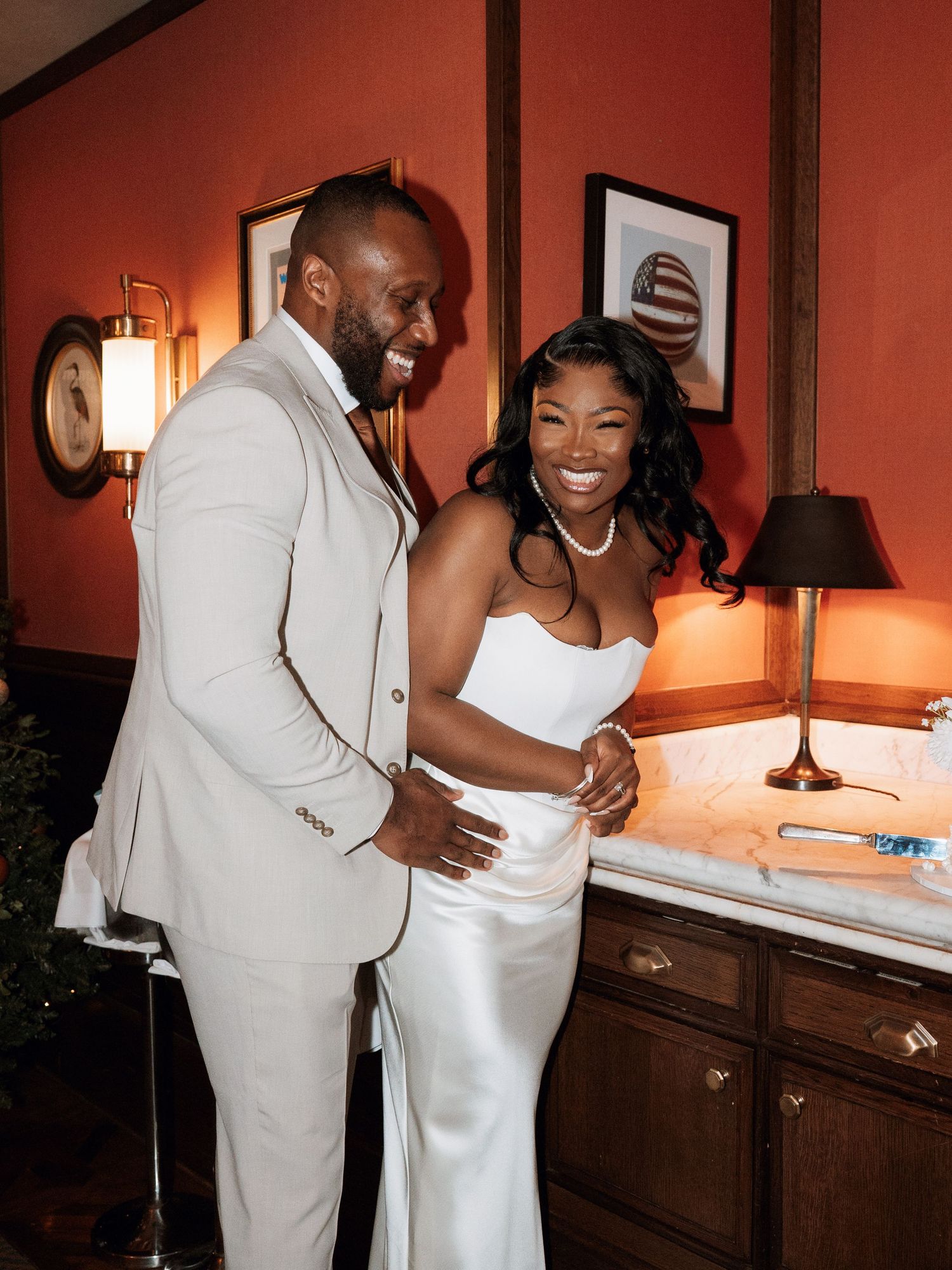 A couple shares a joyful moment in formal attire against warm-toned interior lighting.