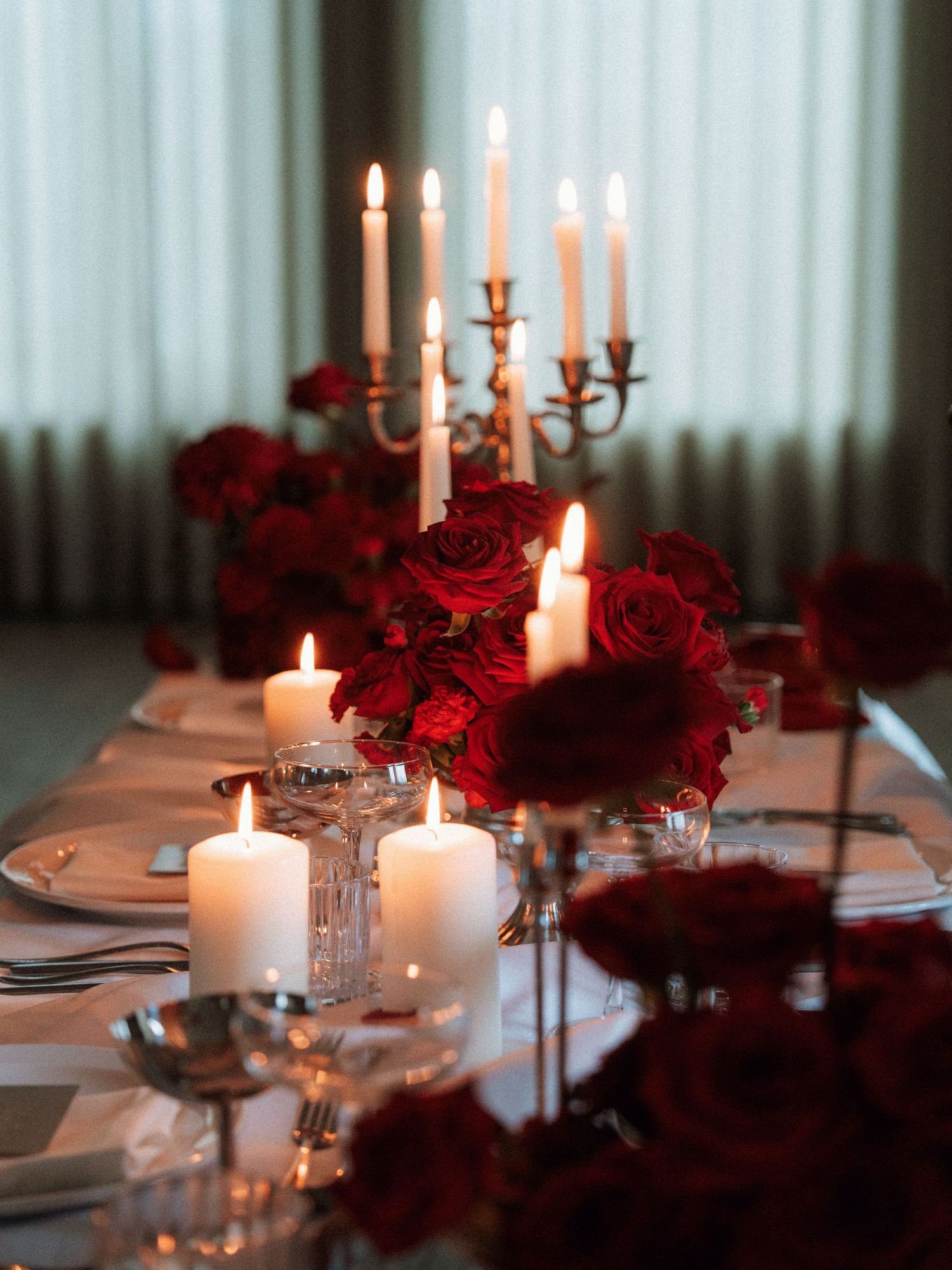 Elegant table setting with white candles and deep red roses in crystal vases creating a romantic dining atmosphere.