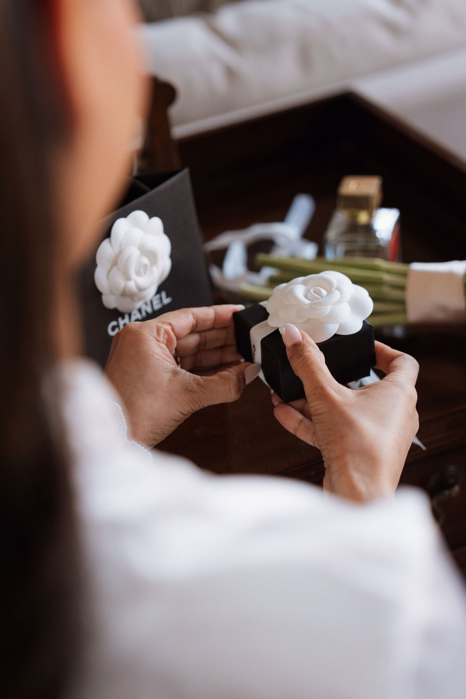 Hands holding white Chanel camellia flower accessories against a dark background.