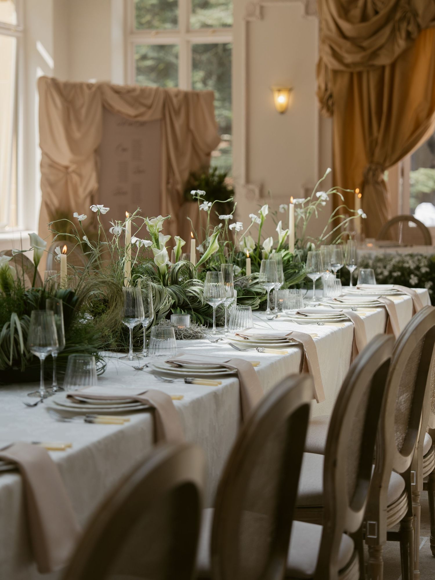 Elegant wedding reception table with white calla lilies, candles, crystal glasses, and linen runner in a grand ballroom.