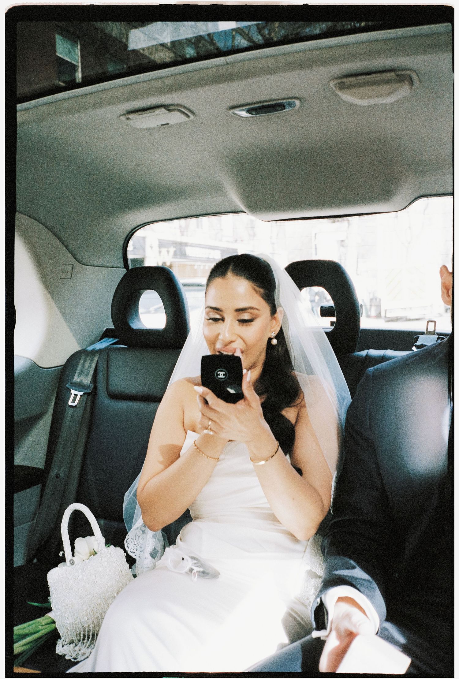 Emotional bride wipes tears with tissues while sitting in back seat of wedding car.