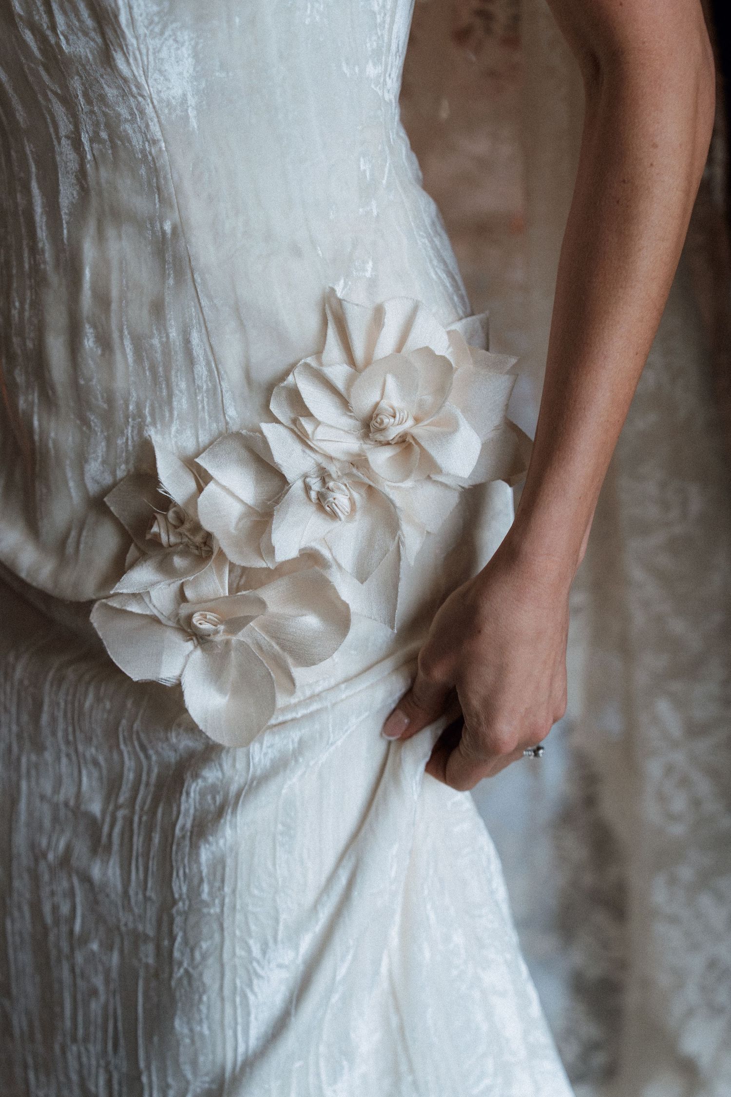 Close-up view of a white wedding dress with delicate floral appliques and ruched fabric details.