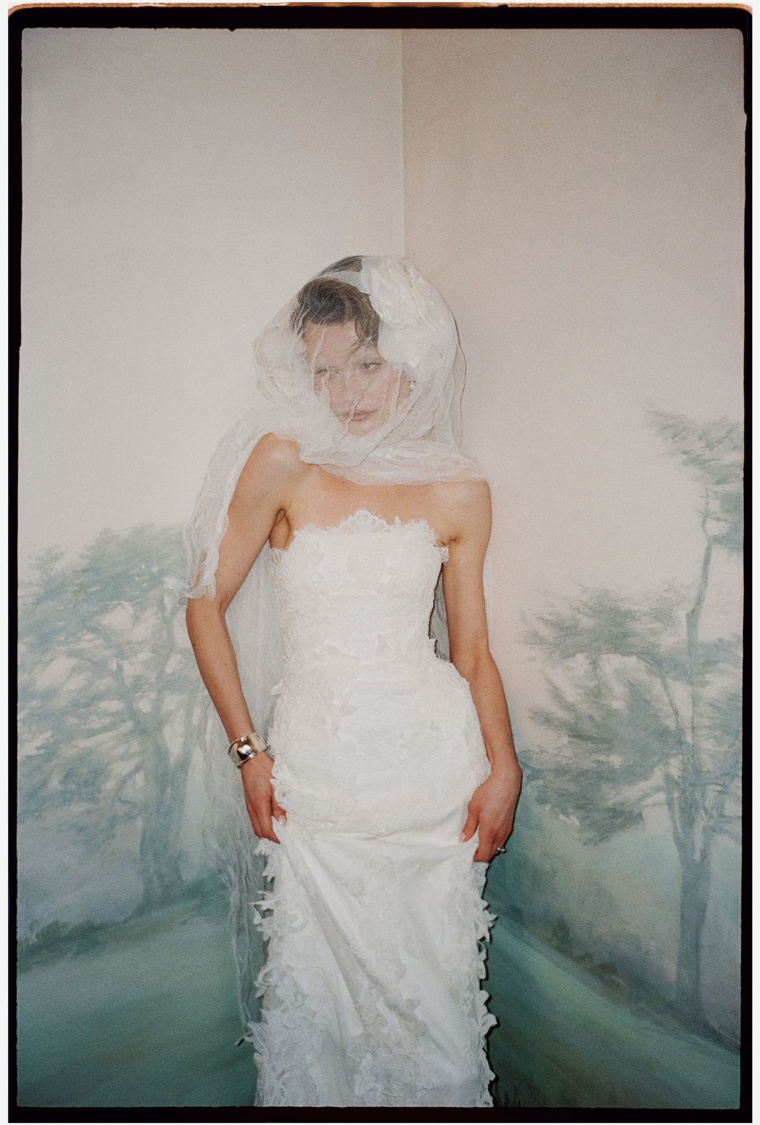 Bride in white wedding dress against muted green and white background.