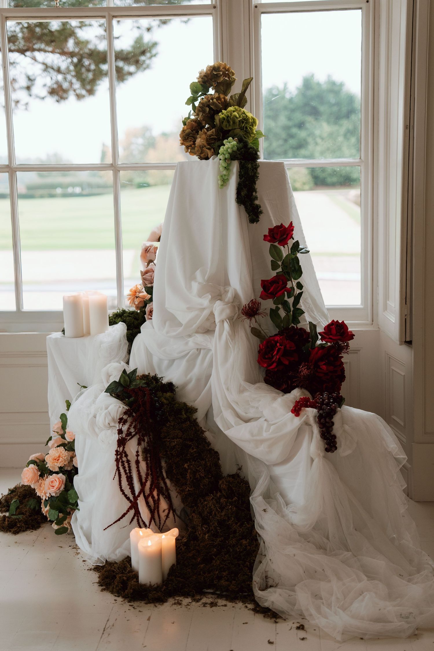 Romantic wedding scene with flowing white fabric, candles, and floral arrangements by a window.
